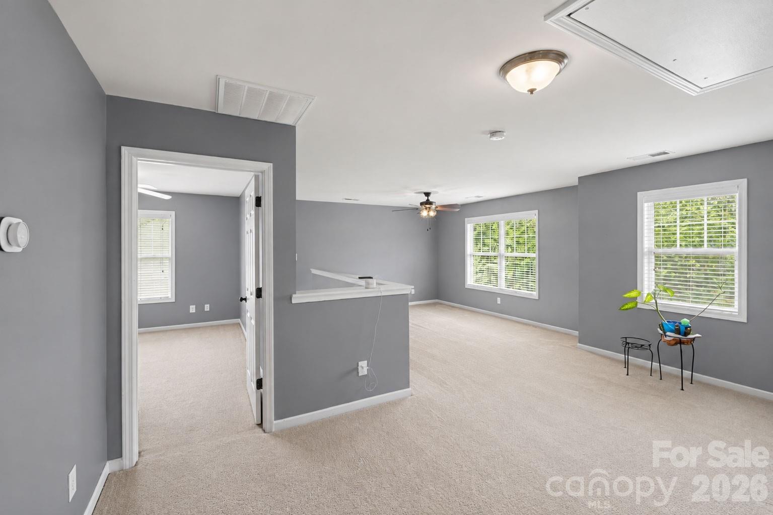 Main-floor primary bedroom with gray walls, beige carpet, and windows overlooking greenery.