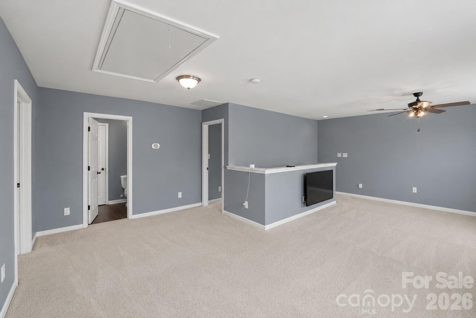 Primary bedroom with light carpet, blue-gray walls, ceiling fan, and a half wall with a television.
