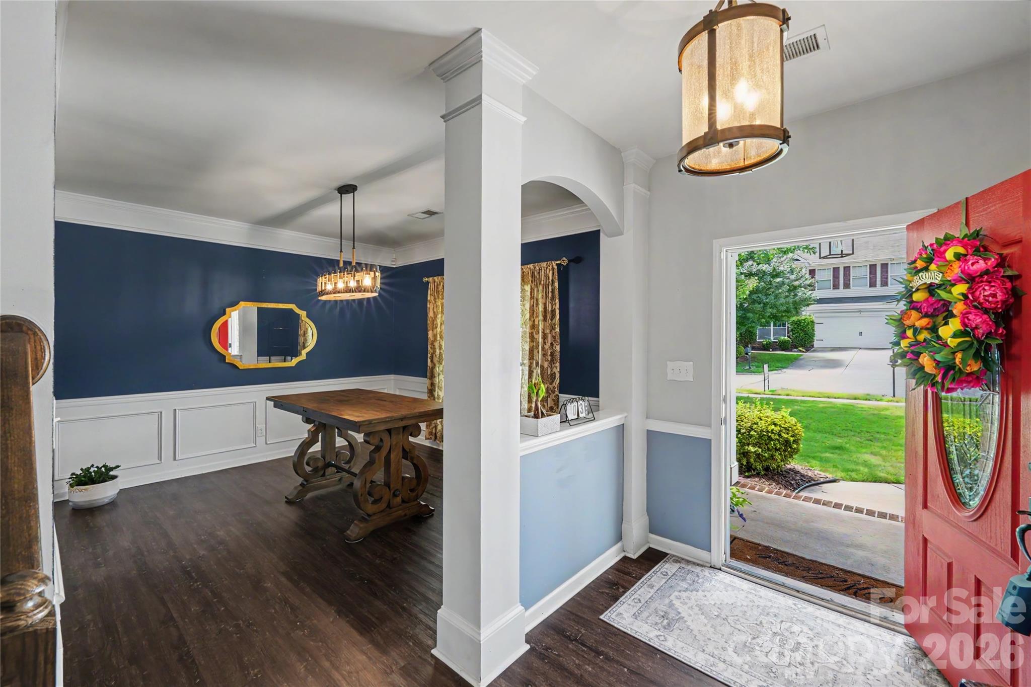 Entry foyer opening to a navy-accented dining room, with a red front door and floral wreath.