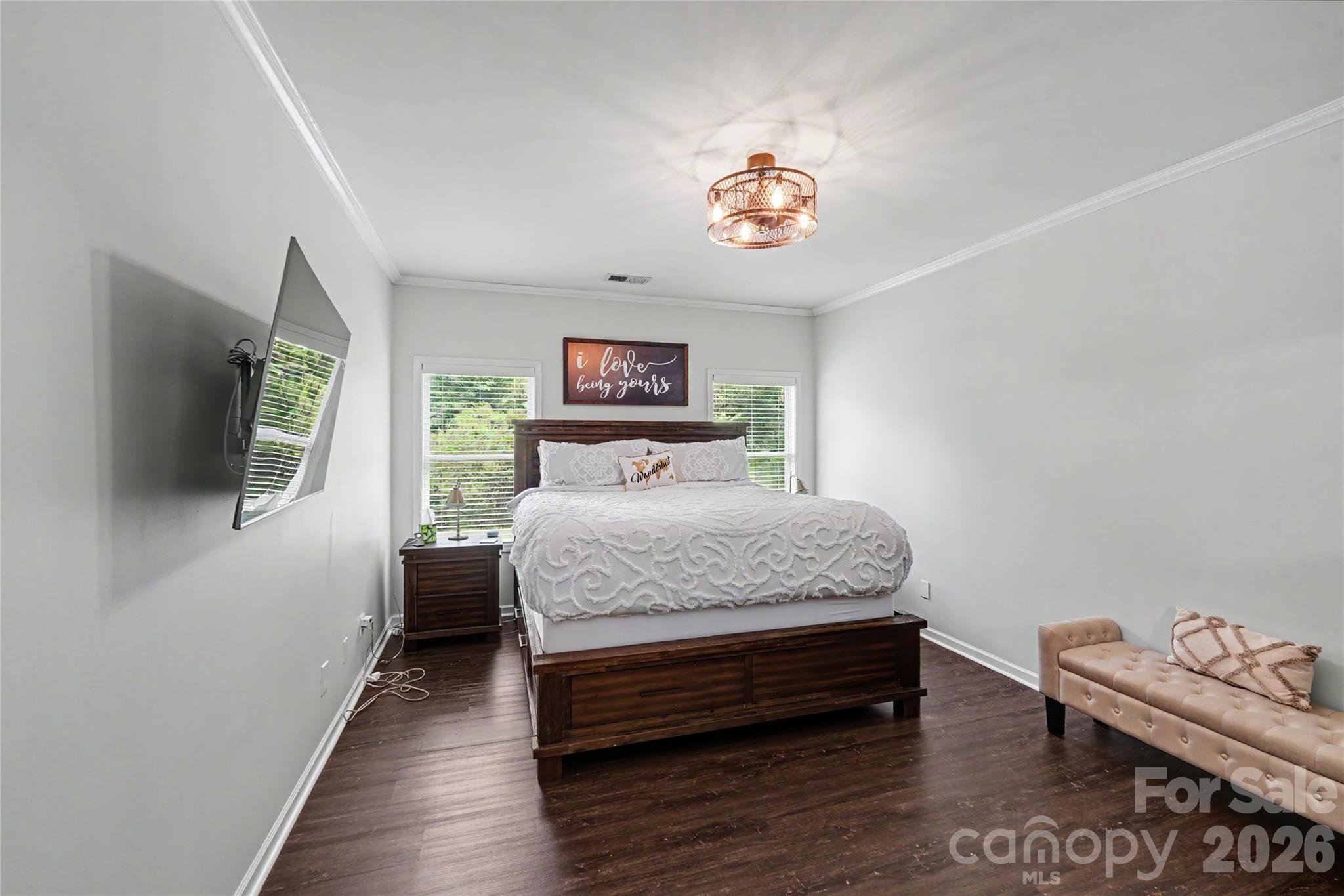 Primary bedroom with white patterned bedding, dark wood furniture, and a beige chaise lounge.