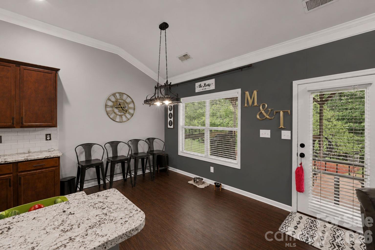 Kitchen and dining area with granite counter, metal bar stools, and a dark accent wall.