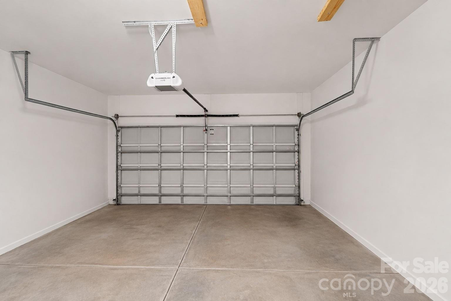 Empty garage with a closed sectional door, concrete floor, and overhead opener.