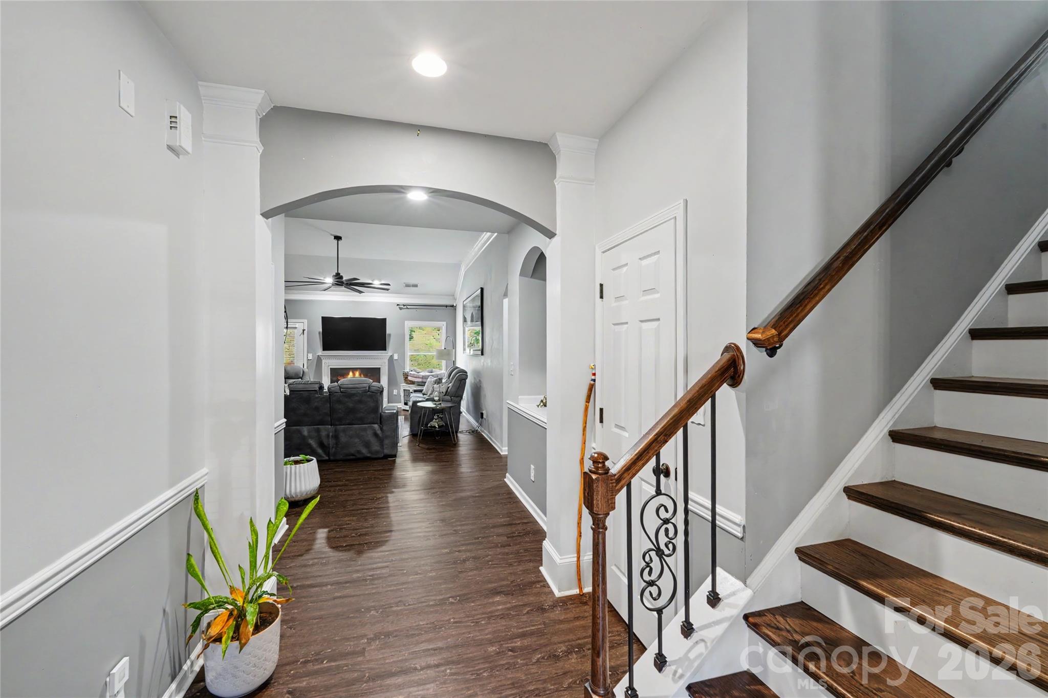 Entry hall with dark wood floors and staircase opening to a furnished living room.