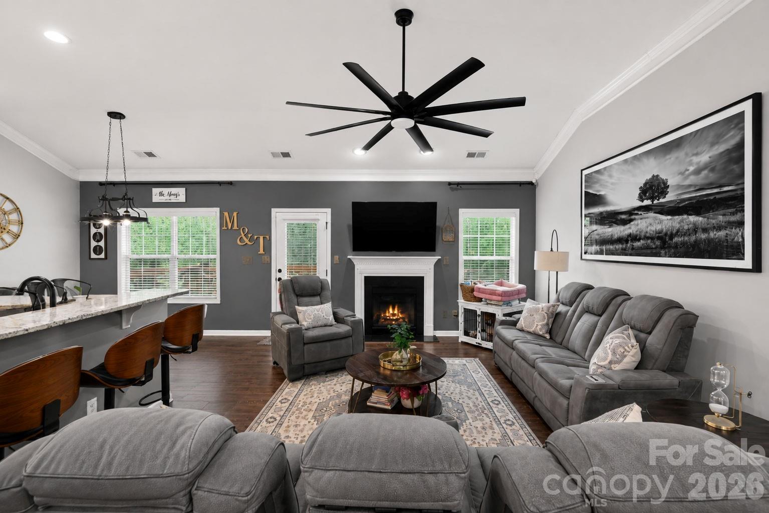 Furnished living room with gray sectional, fireplace, wall-mounted TV, and oversized black ceiling fan.