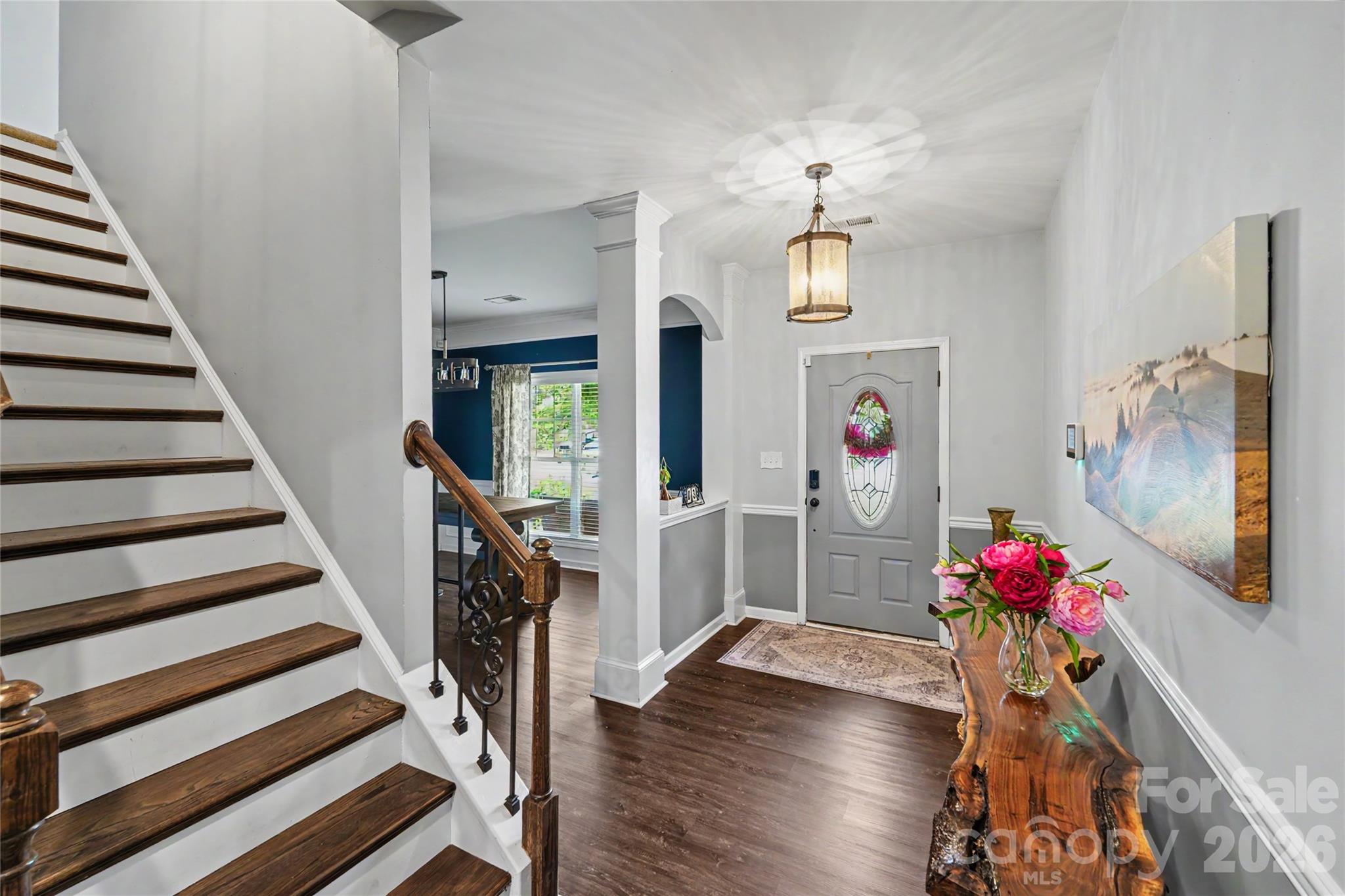 Foyer with a dark wood staircase, stained-glass front door, and live-edge console table with pink flowers.
