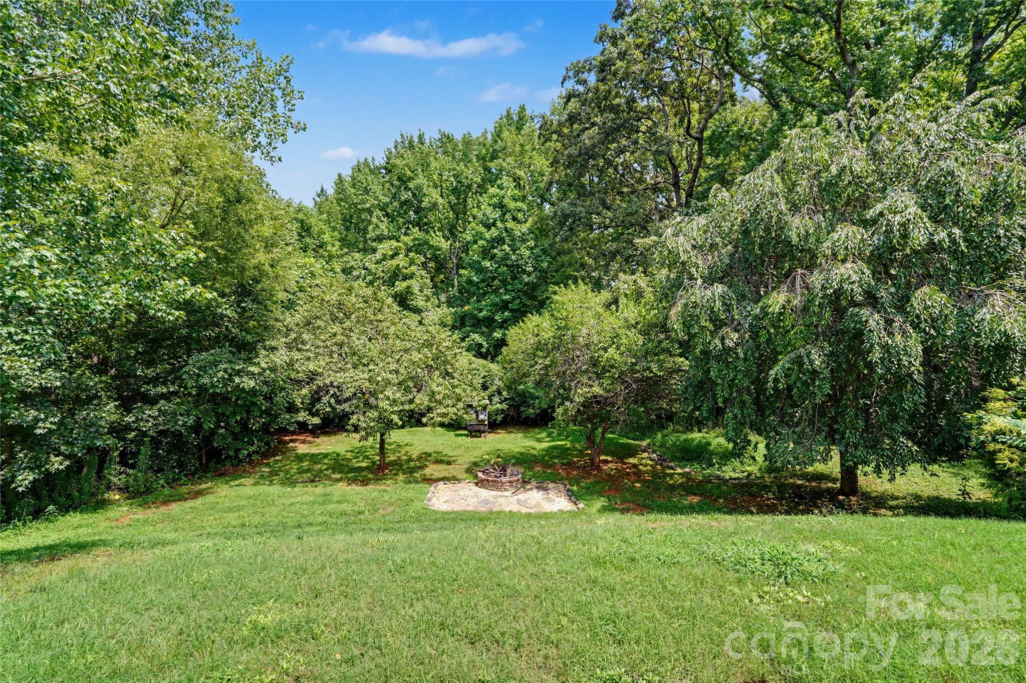 Backyard with a grassy lawn, mature trees, wooded privacy, and a stone-bordered fire pit.