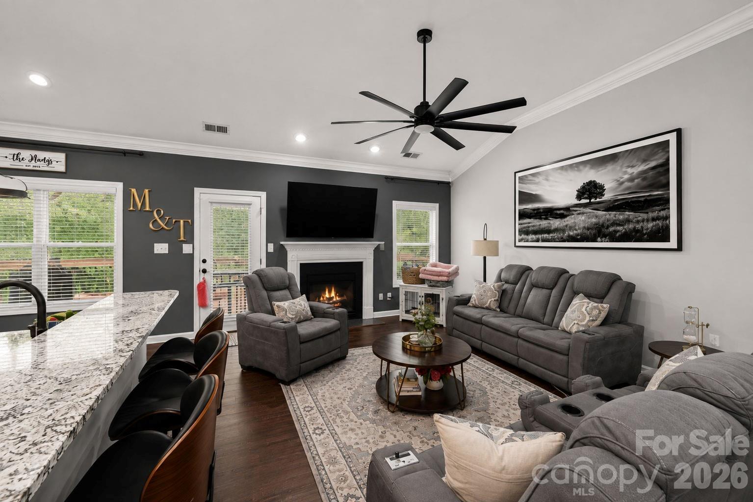 Living room with a fireplace, gray sectional, recliner, and adjoining kitchen island.