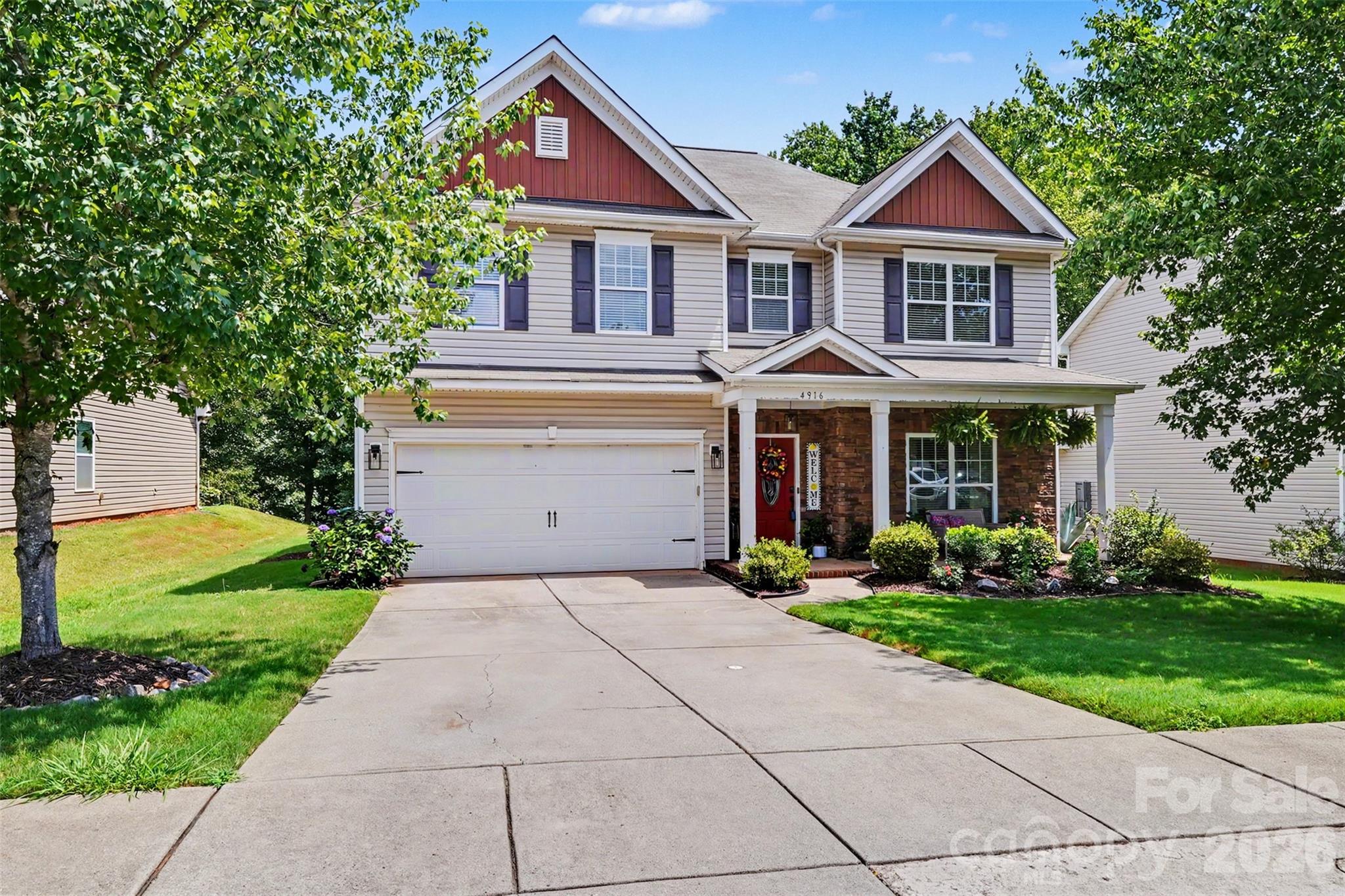 Two-story house with red gables, a covered porch, landscaped yard, and wide driveway.