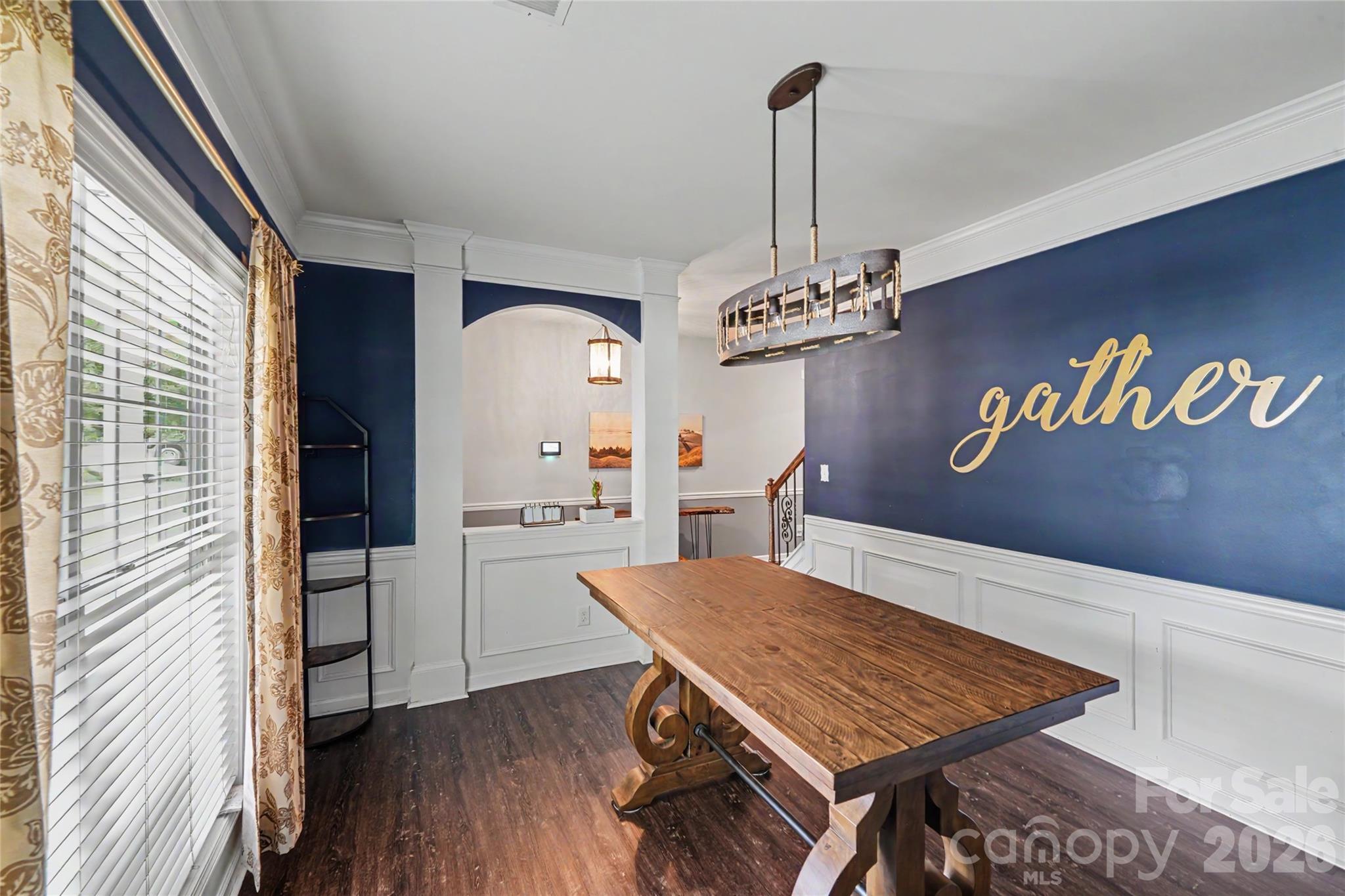 Dining room with a rustic wood table, navy walls, and gold “gather” lettering.