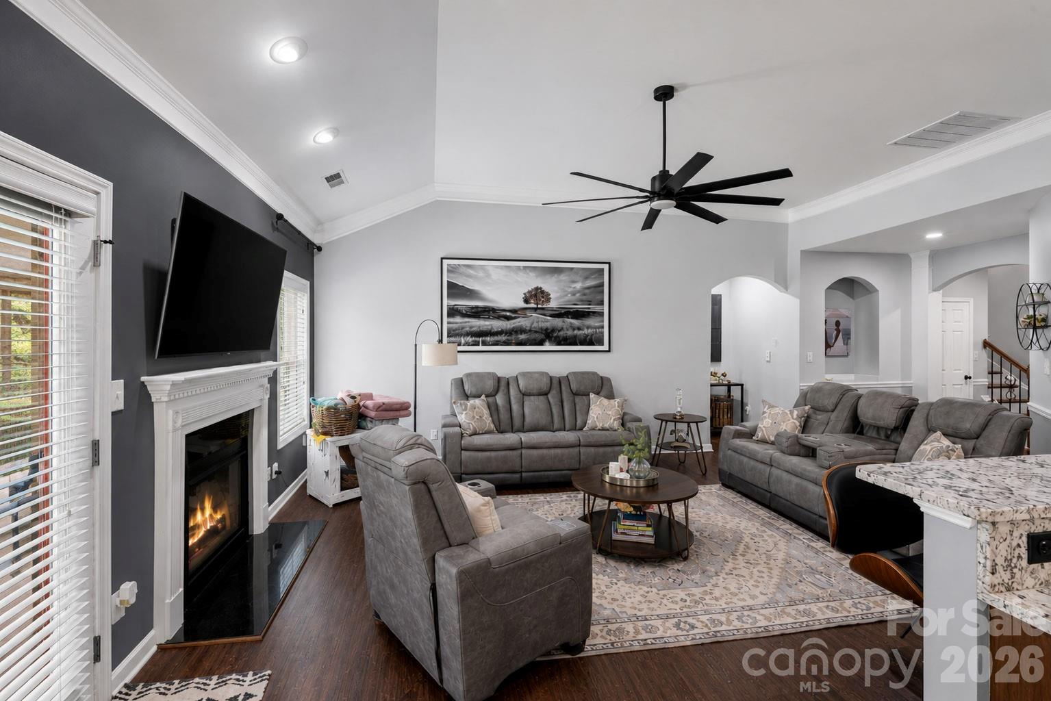 Furnished living room with gray reclining sofas, a fireplace, mounted television, and vaulted ceiling.