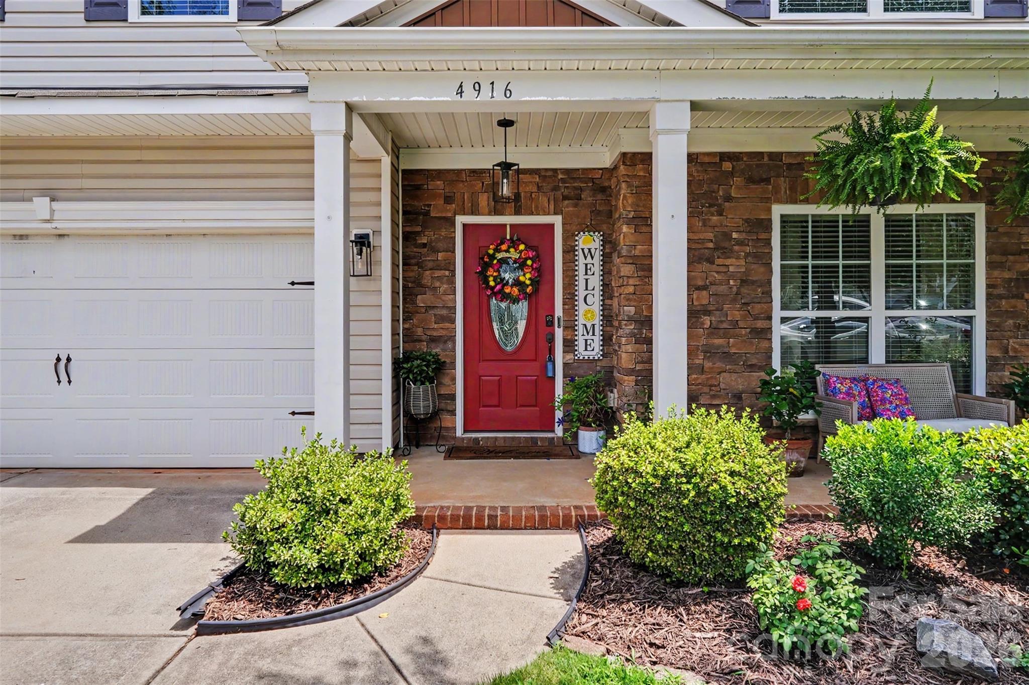 House entrance with a red wreath-decorated door, stone facade, covered porch, and landscaped shrubs.