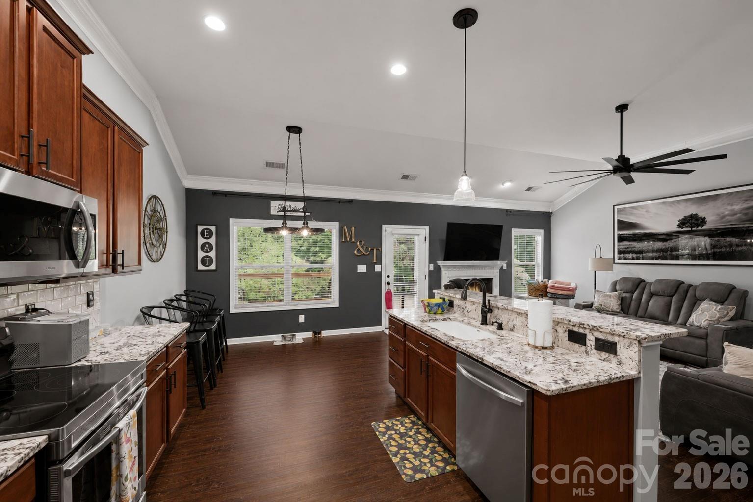 Kitchen with dark wood cabinets, granite island, stainless steel appliances, and an adjoining living area with a fireplace.