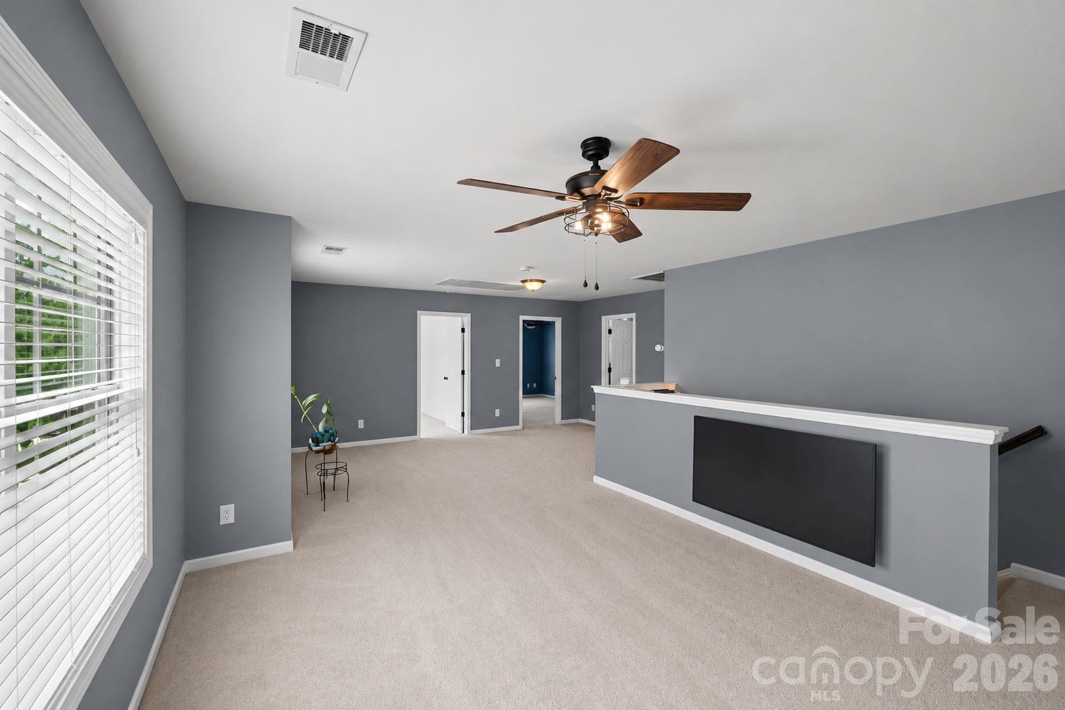 Primary bedroom with gray walls, a wood-blade ceiling fan, and a half wall overlooking the stairs.