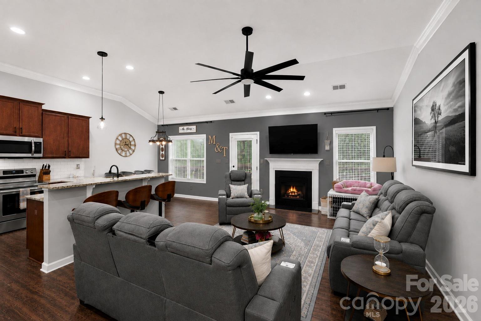 Open-plan living room and kitchen with gray sofas, a fireplace, and a large island with bar seating.