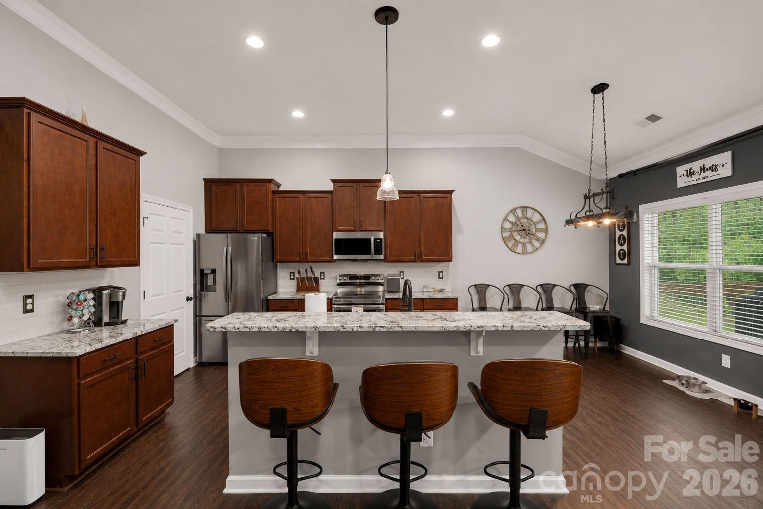 Kitchen with dark wood cabinets, stainless appliances, and a large island with three bar stools.