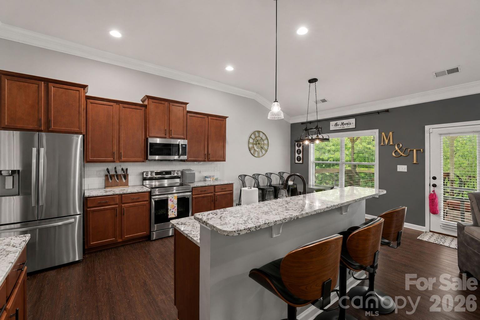 Kitchen with dark wood cabinets, stainless steel appliances, and a large granite island with bar seating.