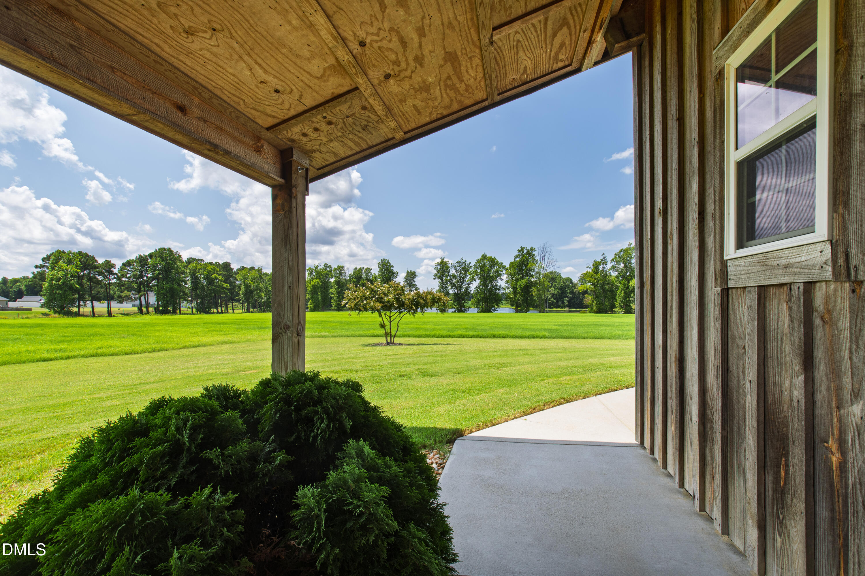 Covered wooden porch overlooking a broad green lawn and distant trees.