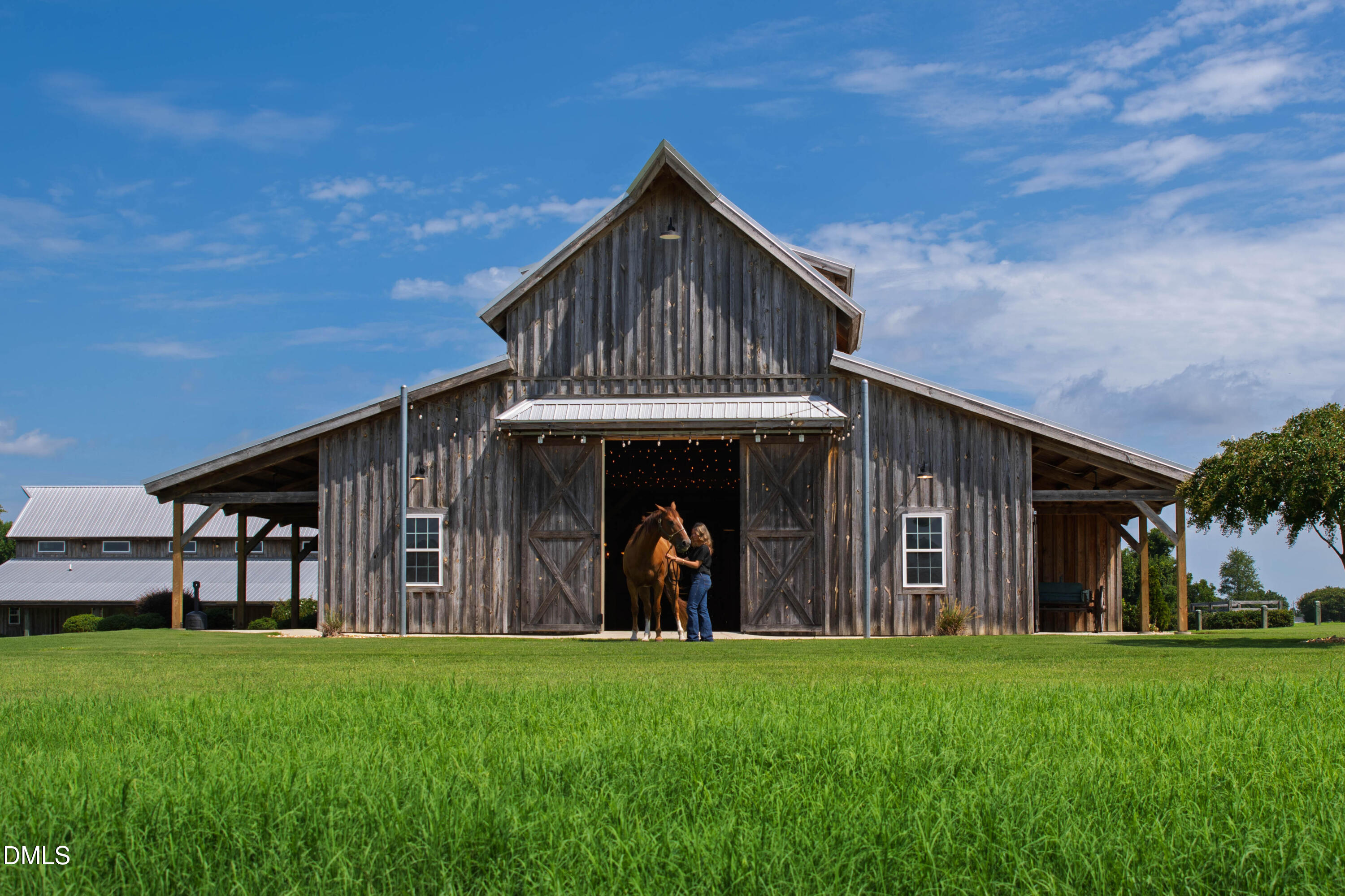 Weathered timber horse barn with a horse and handler standing in its open doorway.
