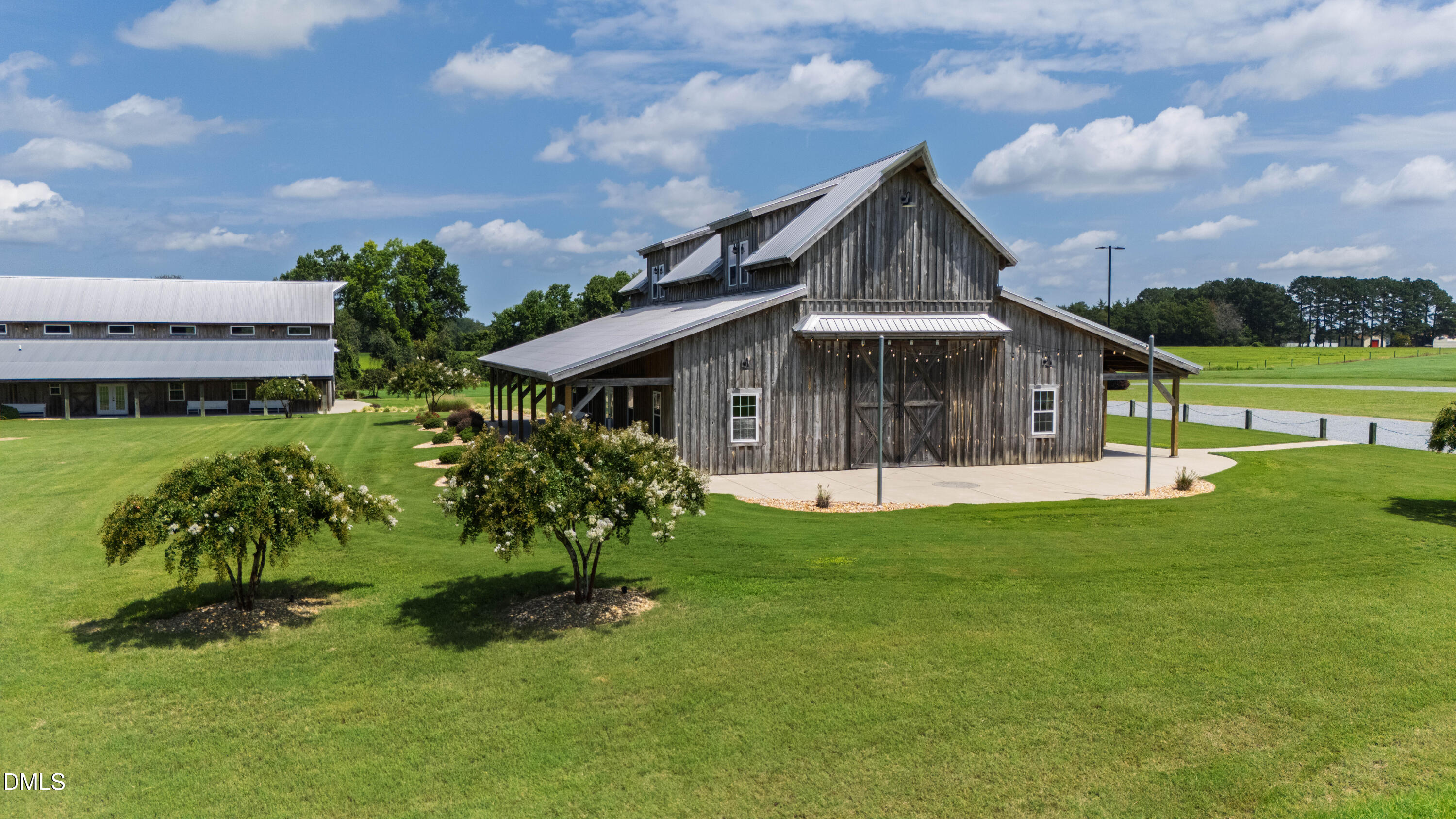 Weathered-wood barn-style building with metal roofs, covered patio, and broad green lawn.
