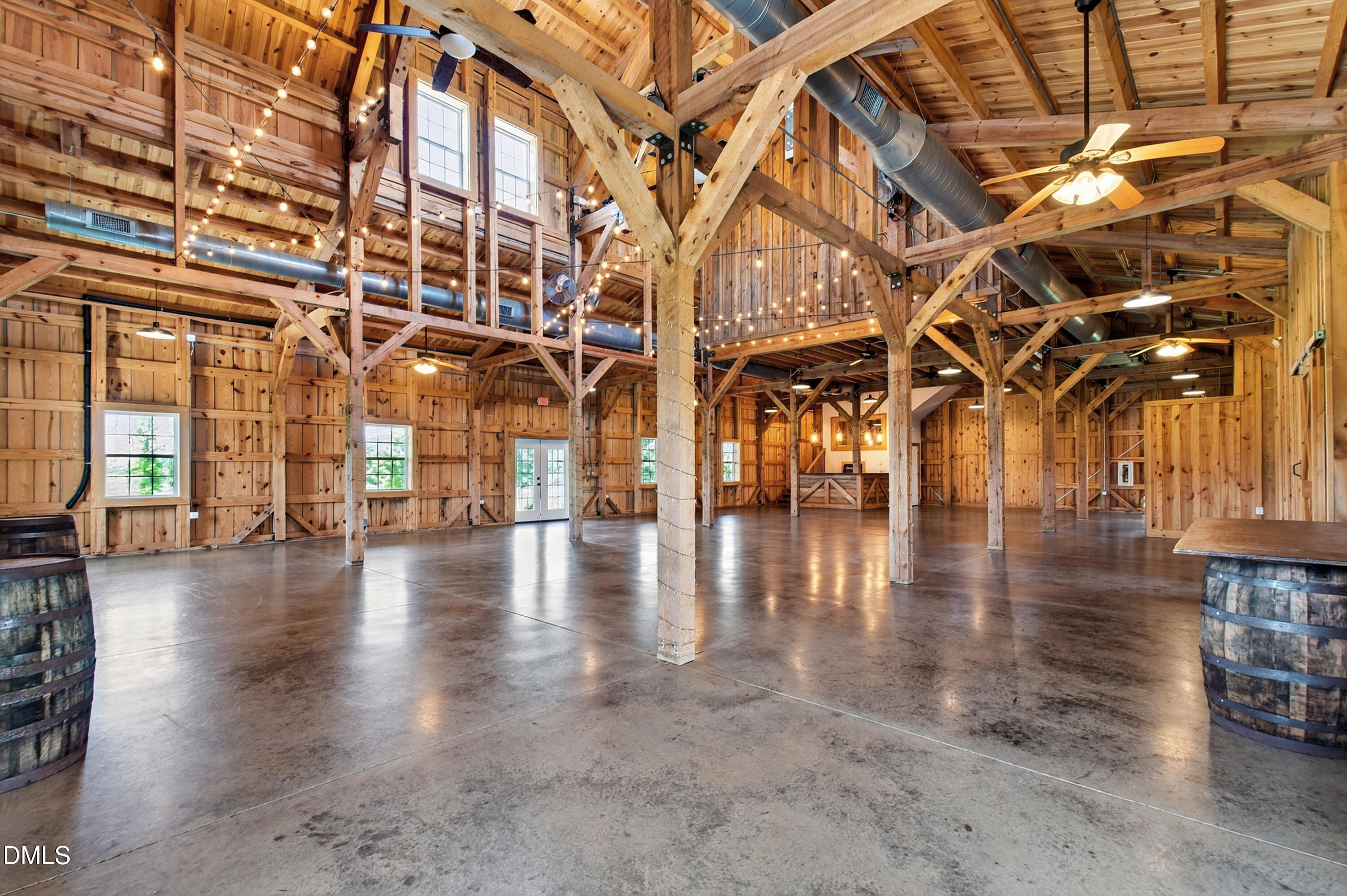 Timber-frame barn interior with exposed beams, string lights, and a spacious polished concrete floor.