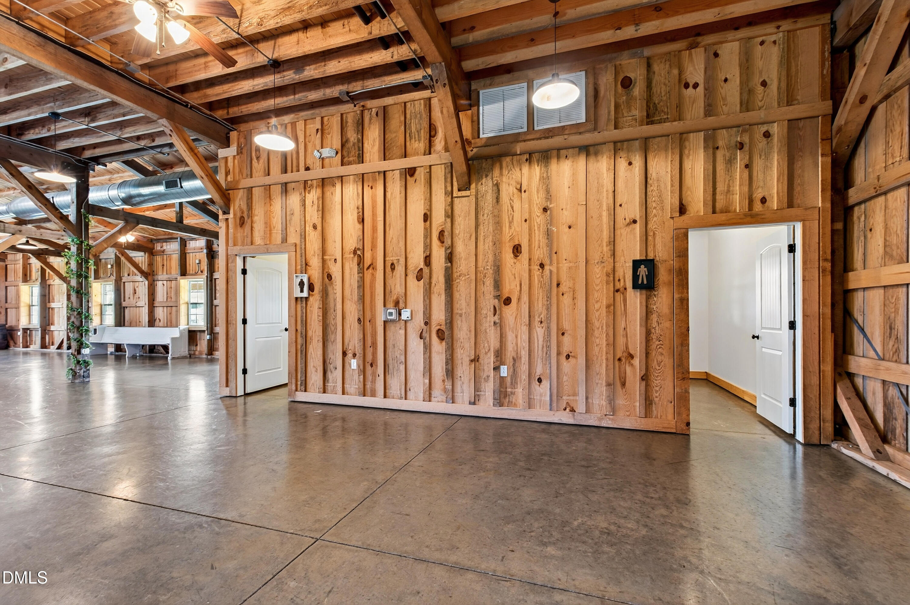 Open timber interior with exposed beams, concrete floors, and restroom doorways.