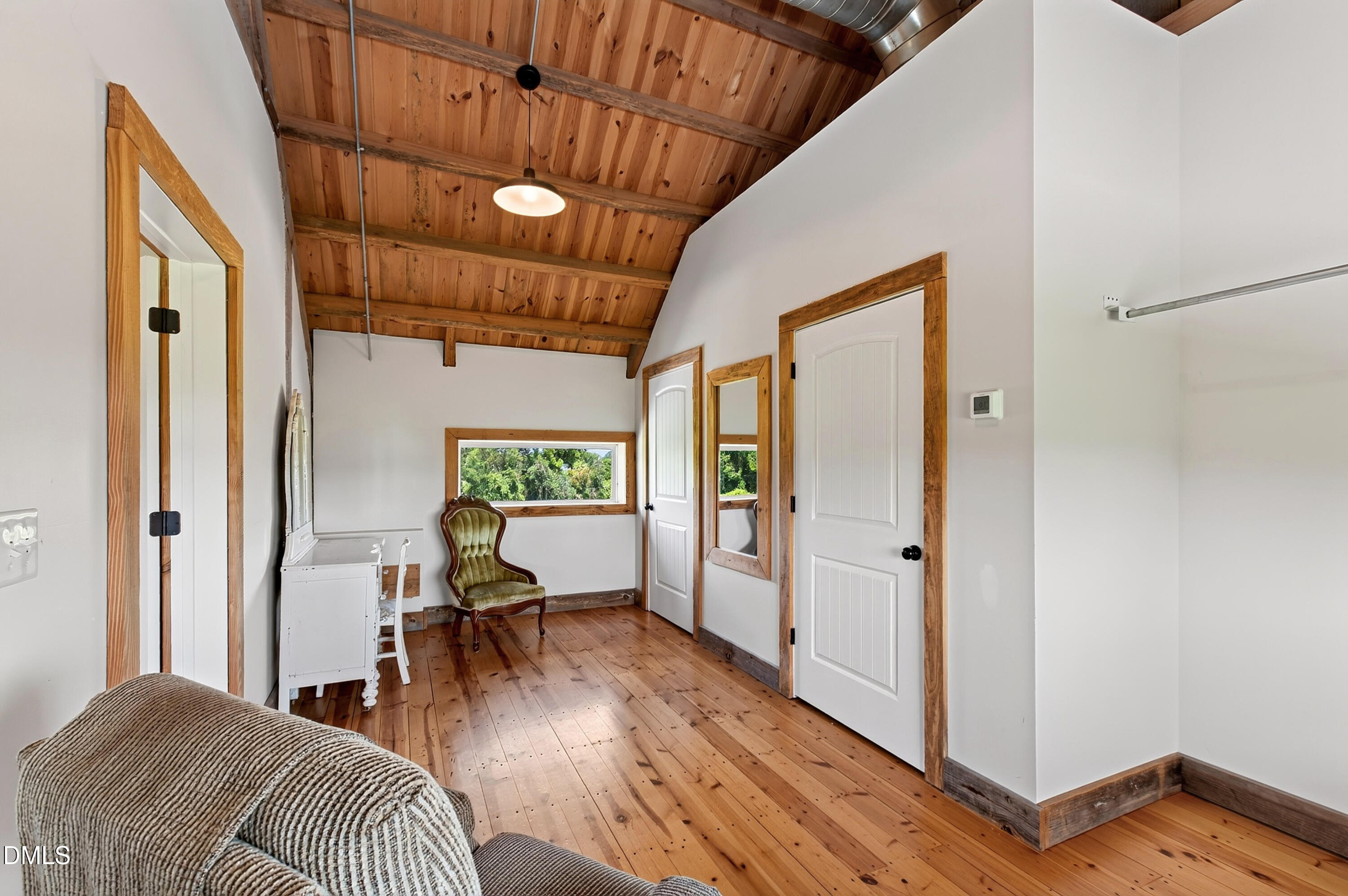 Furnished room with exposed wood ceiling and floors, a vintage chair, and a narrow window overlooking trees.