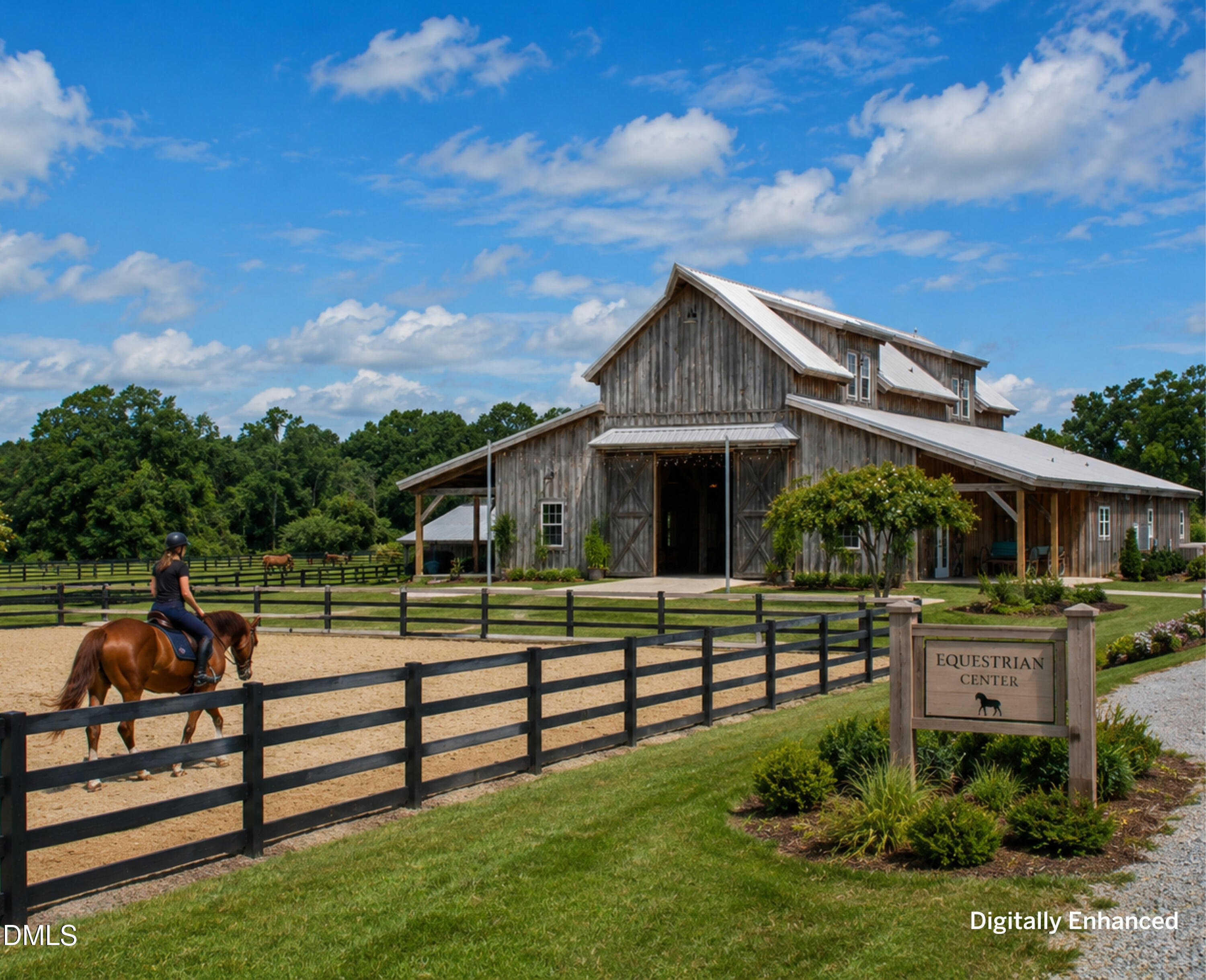 Weathered-wood equestrian barn beside a fenced riding arena, with a horse and rider.