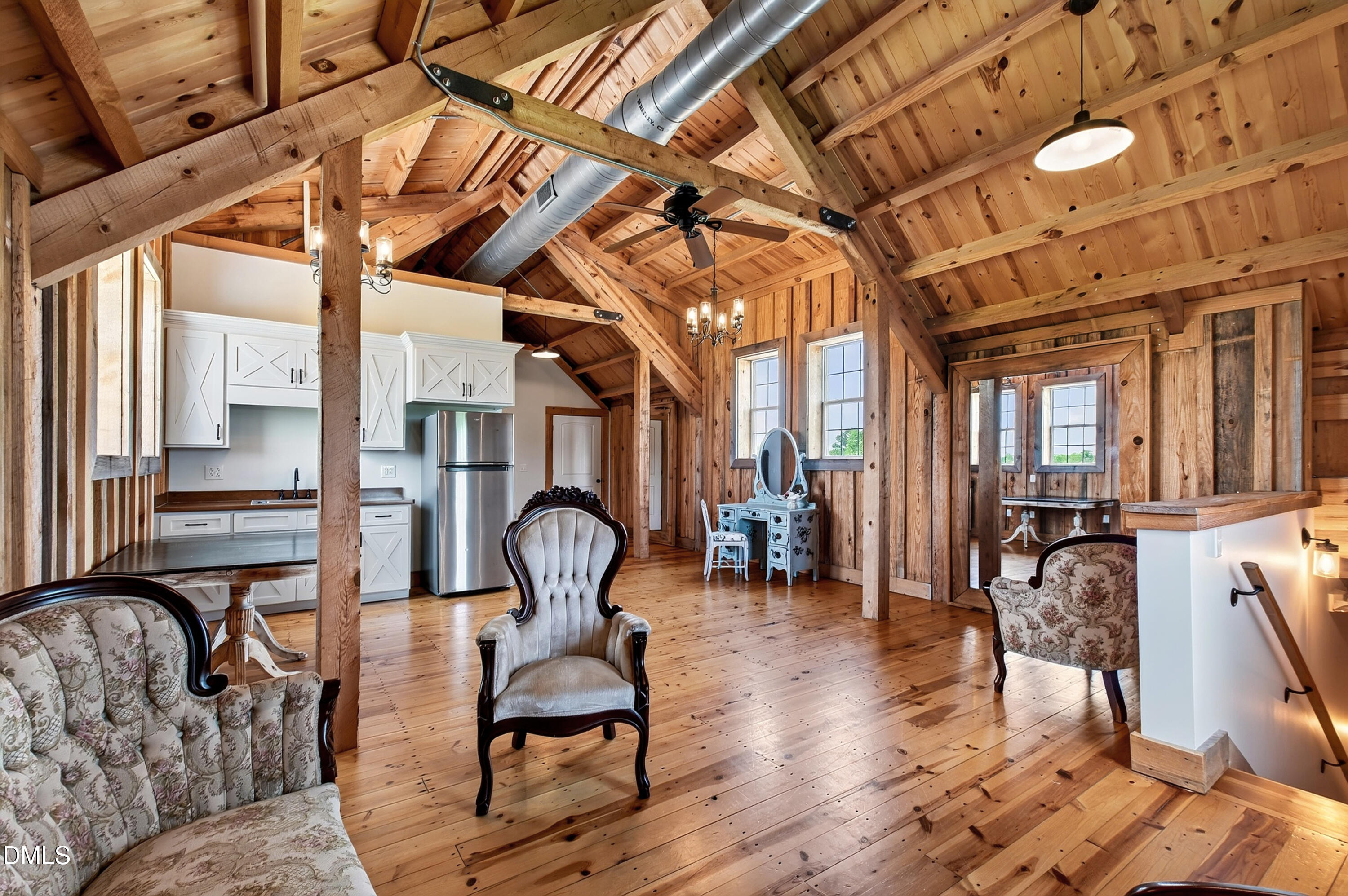 Furnished open-plan living area and kitchen with exposed timber beams, vaulted ceiling, and vintage chairs.