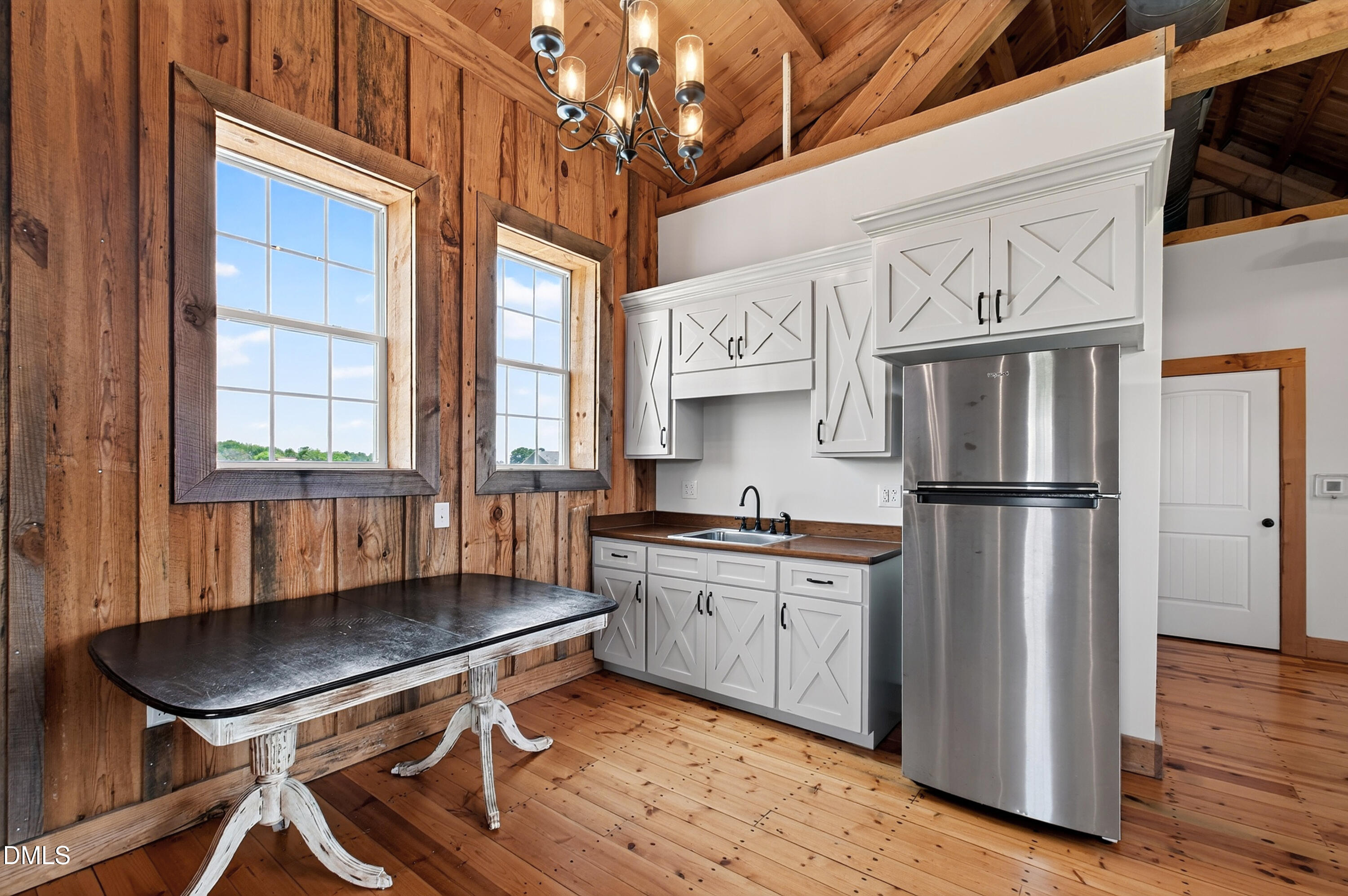 Rustic kitchen with white X-front cabinets, a stainless steel refrigerator, and wood-paneled walls.
