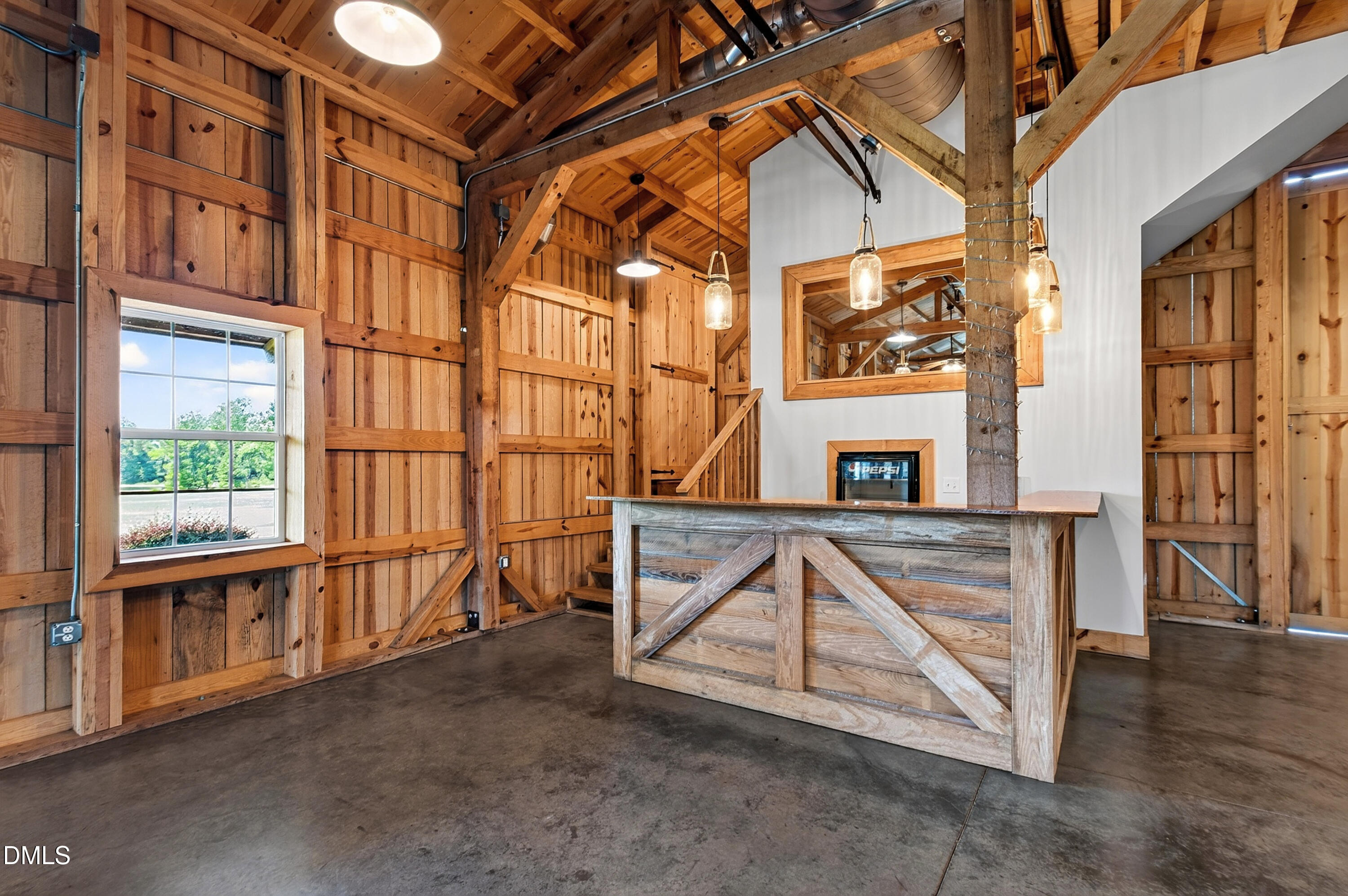 Rustic wood-paneled interior with exposed beams, concrete floor, and a reclaimed-wood counter beside a staircase.
