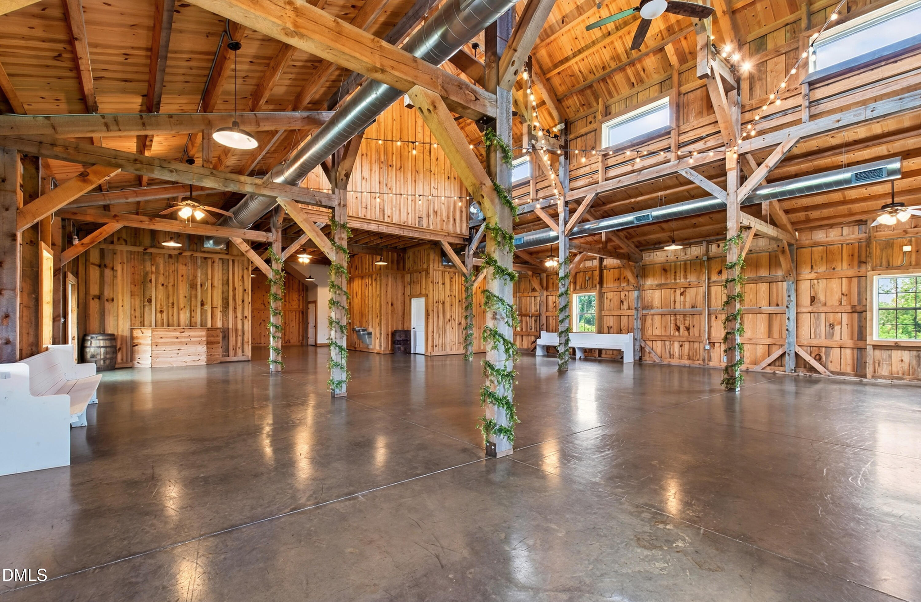 Barn-style event space with exposed timber beams, string lights, and polished concrete floors.