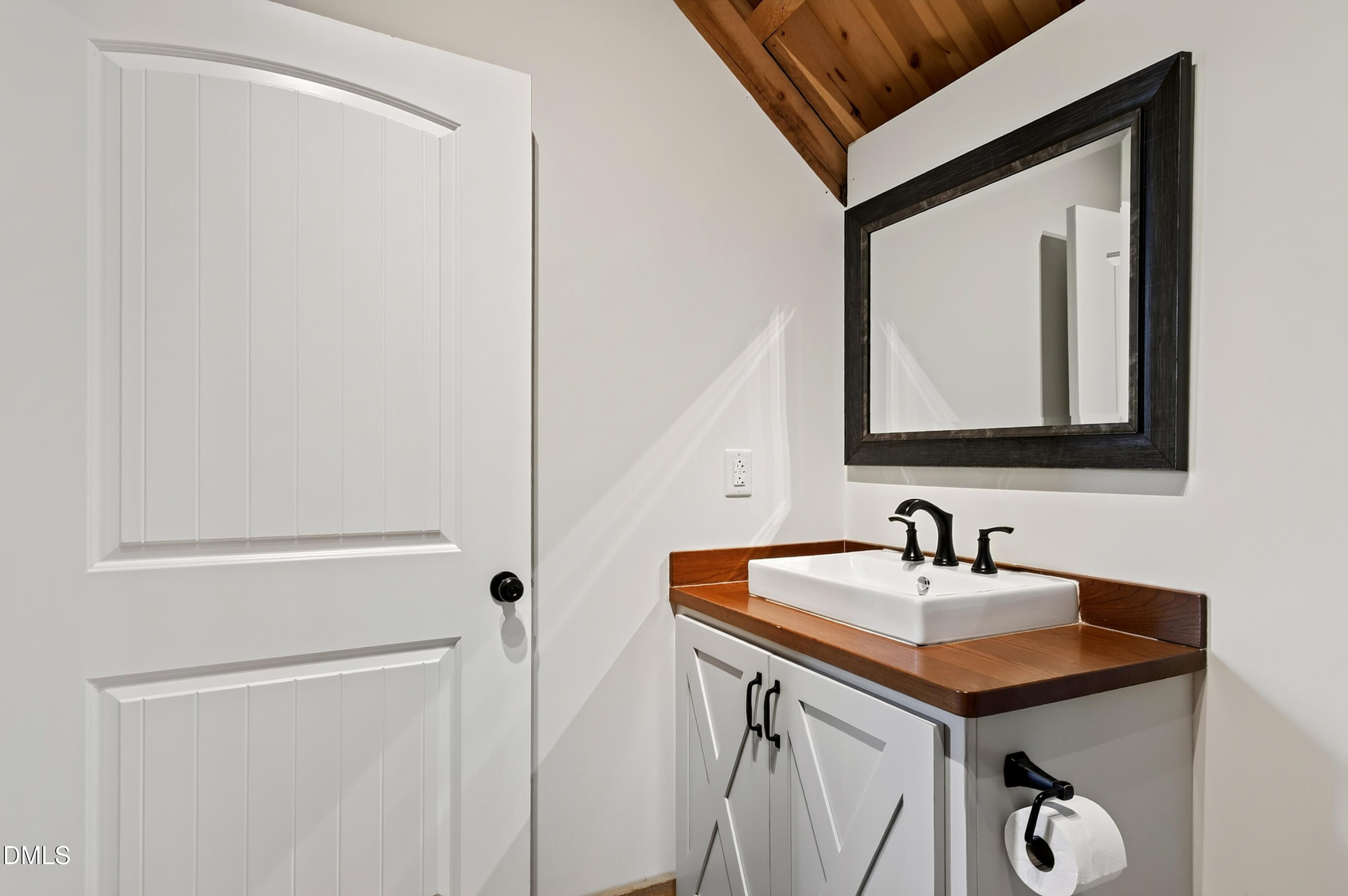 Bathroom vanity with a wood countertop, white vessel sink, black fixtures, and dark-framed mirror.