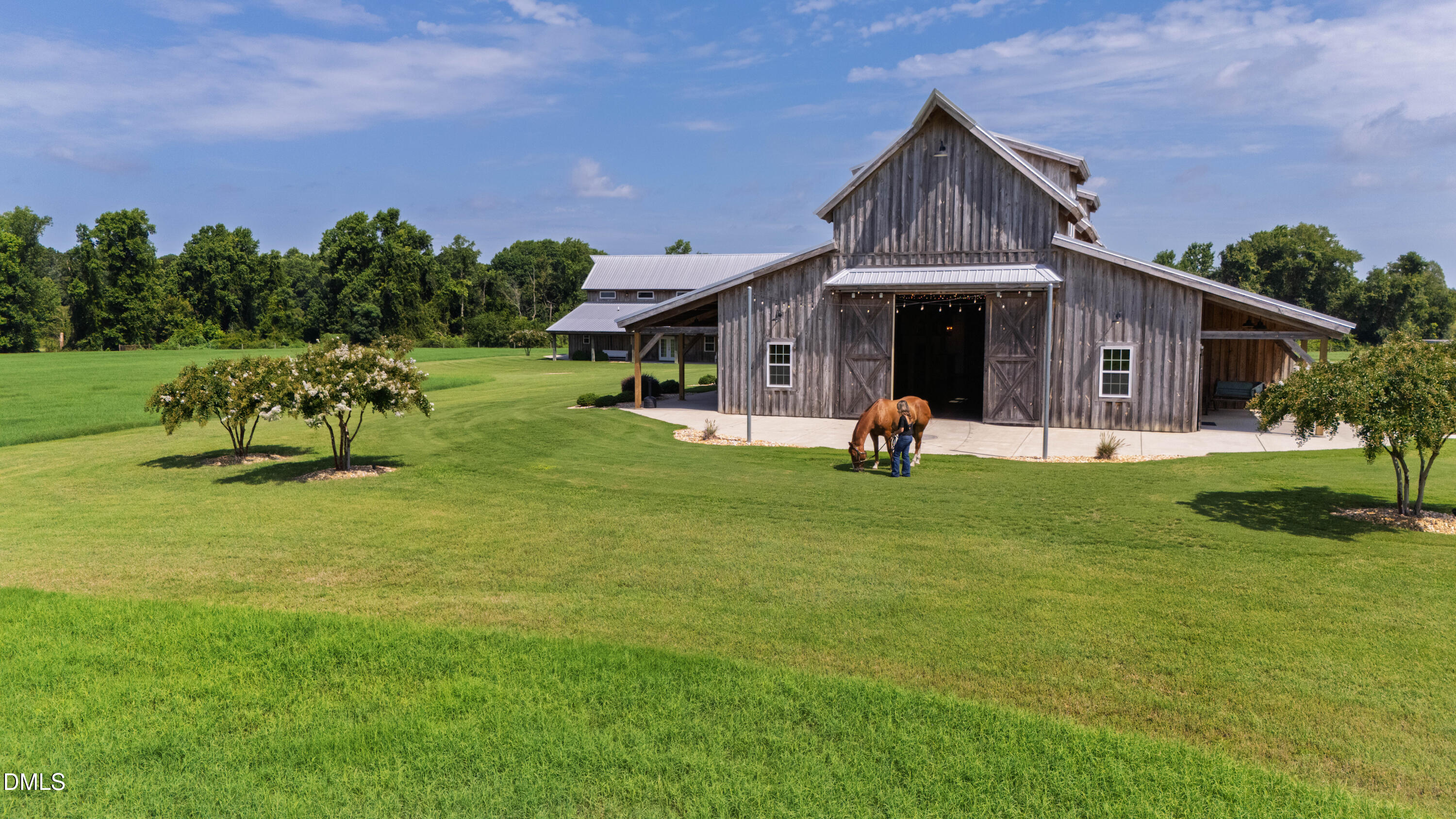 Rustic wooden barn with a metal roof, broad lawn, and a person beside a horse.