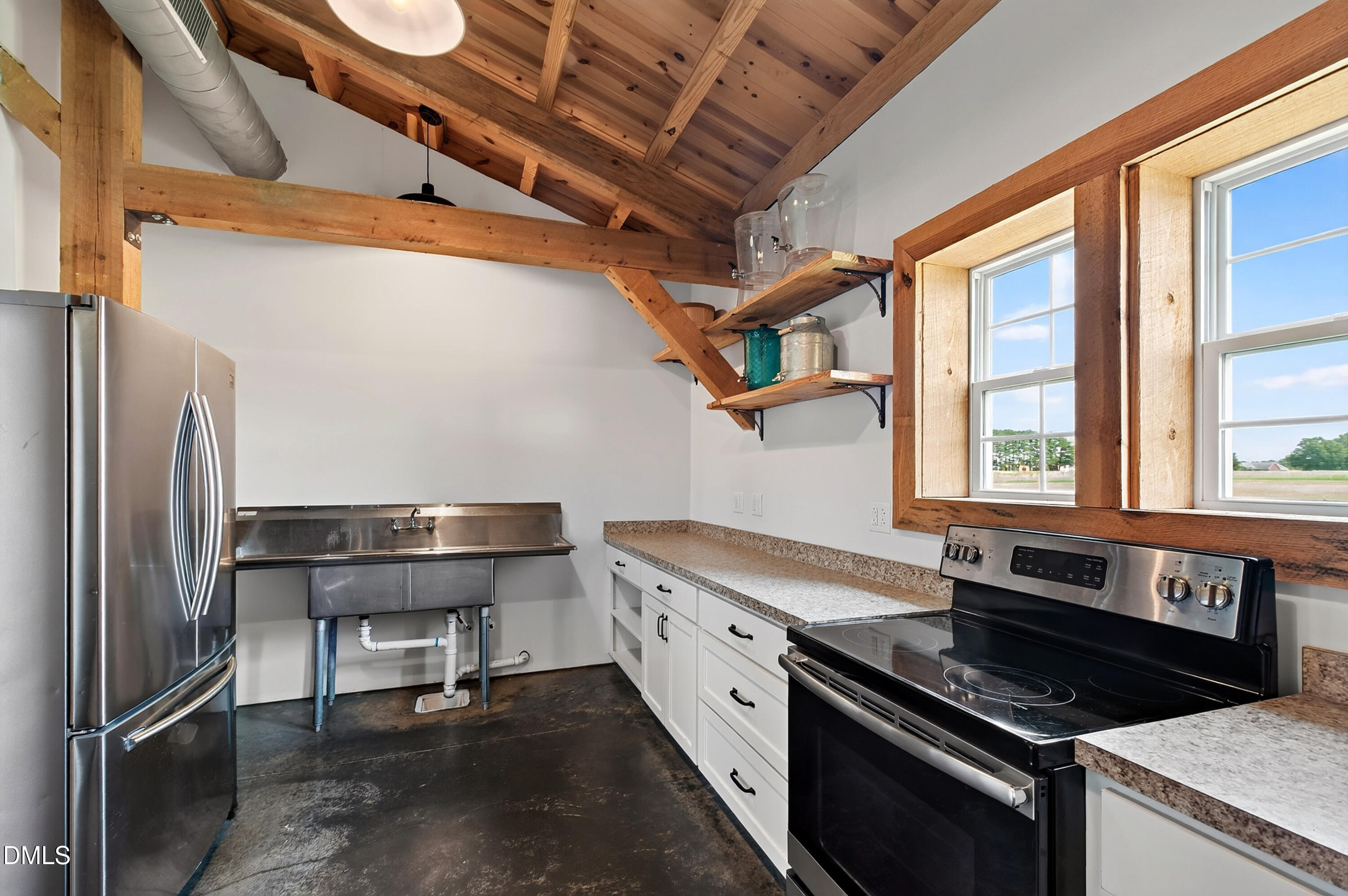 Kitchen with exposed timber ceiling, stainless steel appliances, white cabinets, and windows overlooking open land.