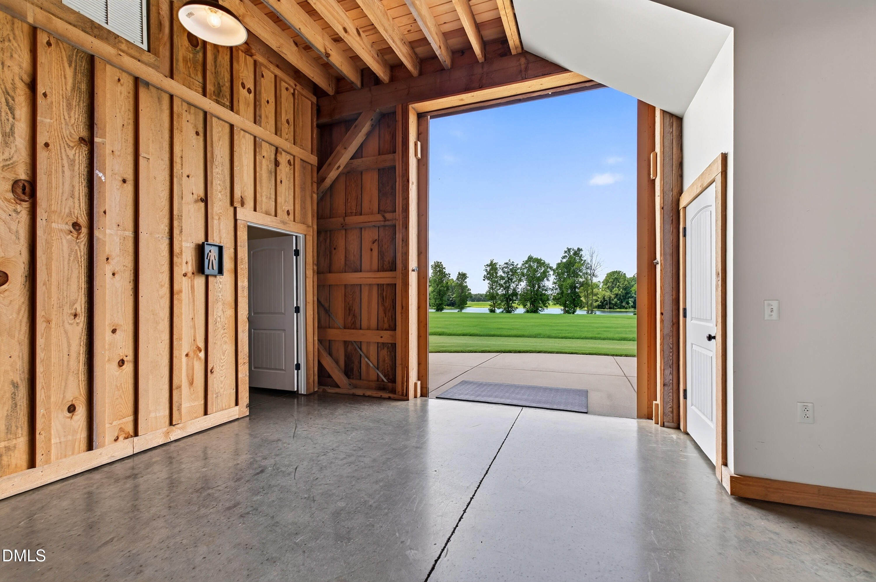 Wood-sided garage with exposed rafters, concrete floor, and open doorway overlooking a lawn and pond.