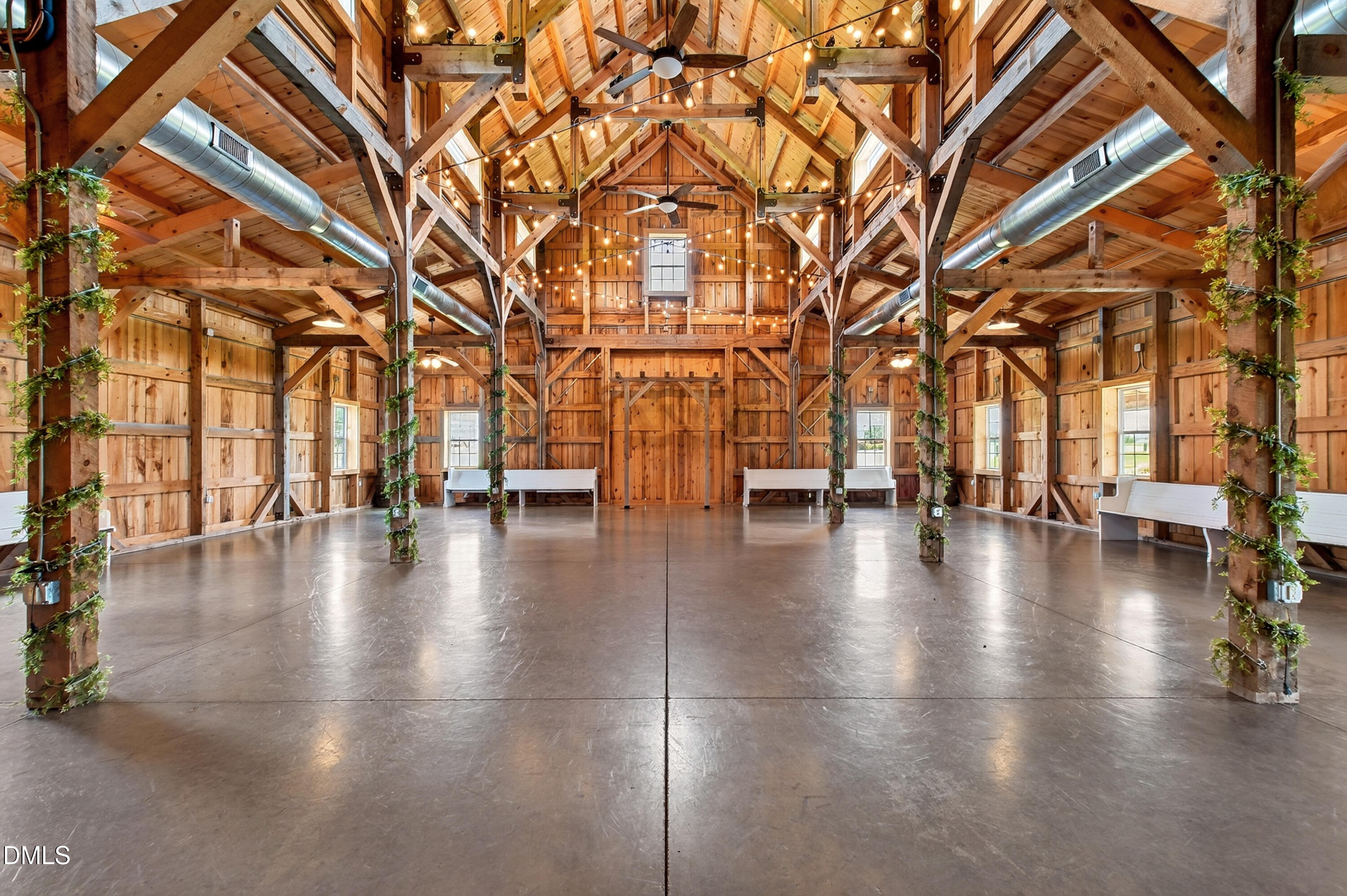 Timber-frame barn interior with exposed beams, string lights, and a polished concrete floor.