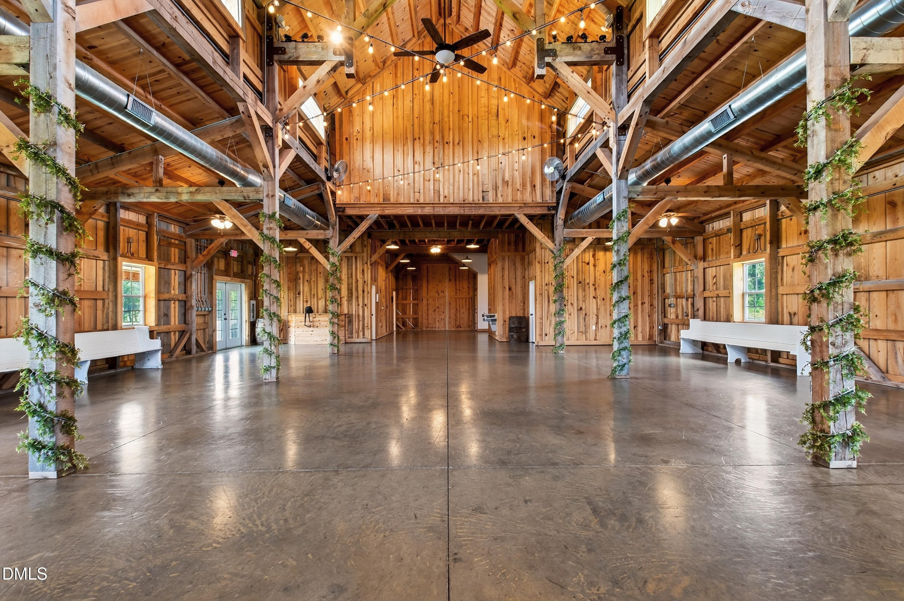 Spacious timber-frame barn interior with exposed trusses, string lights, and a polished concrete floor.