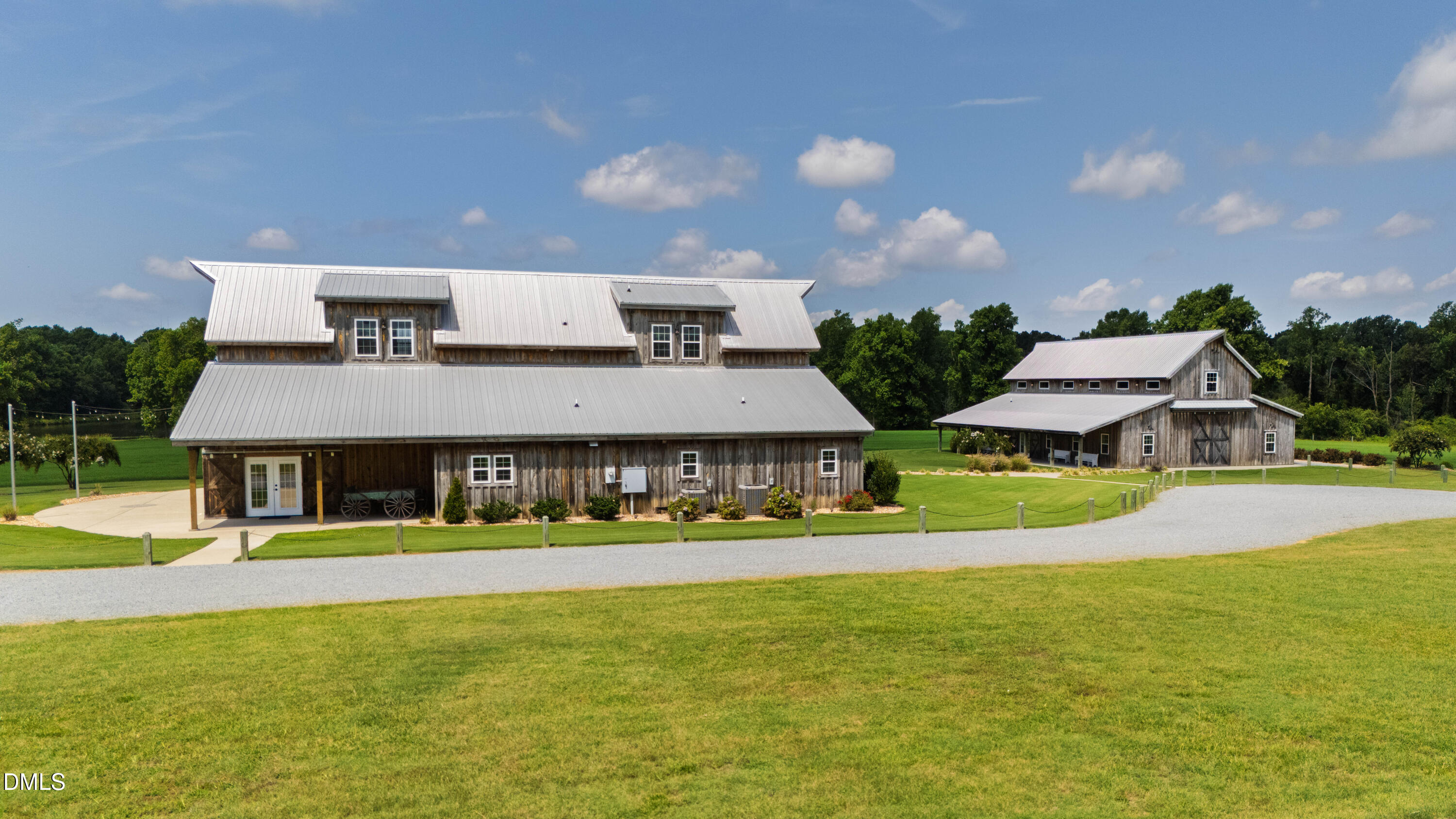 Two rustic wooden buildings with metal roofs beside a gravel drive and broad green lawn.