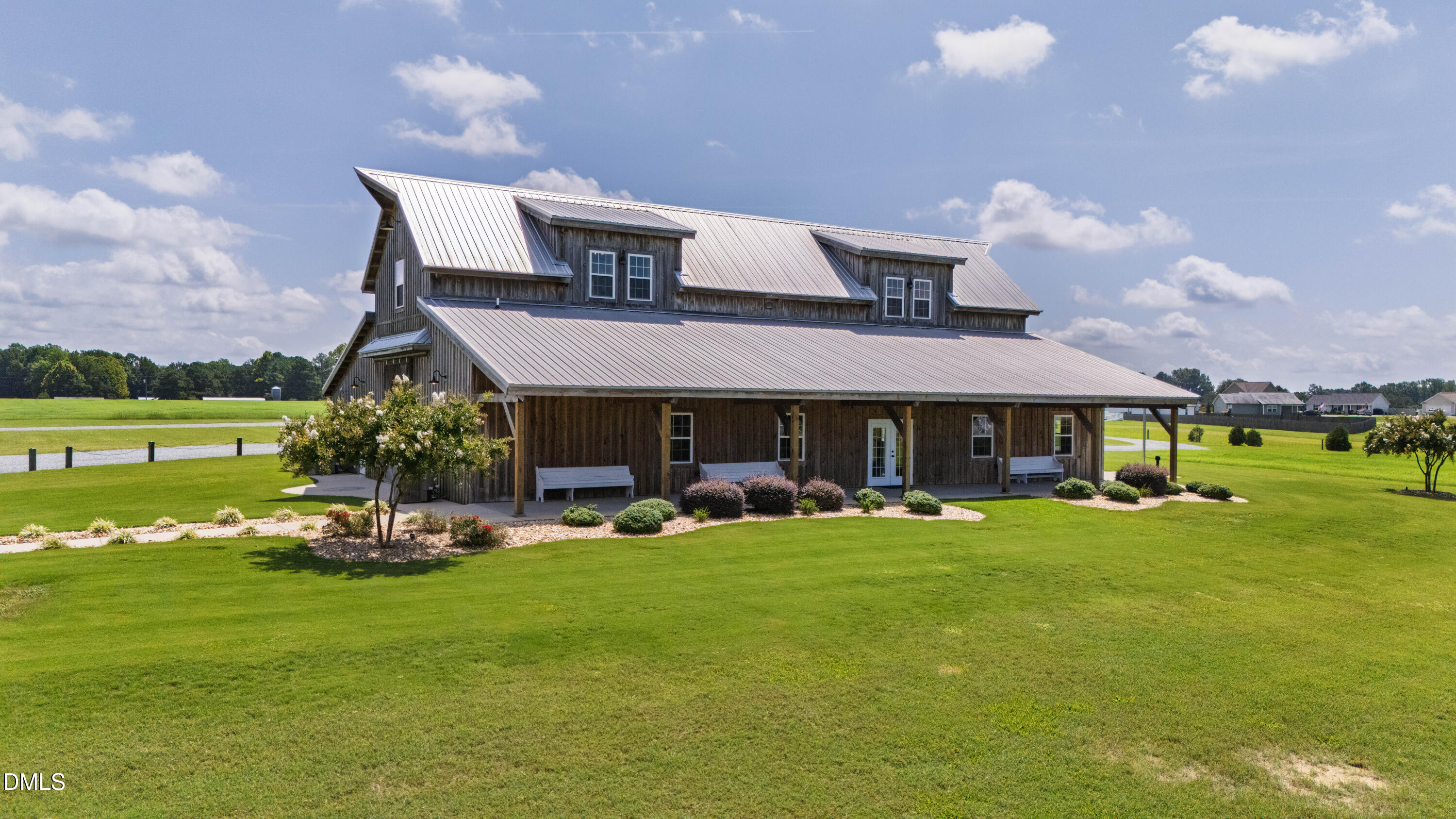 Barn-style home with a metal roof, covered porch, and broad green lawn.