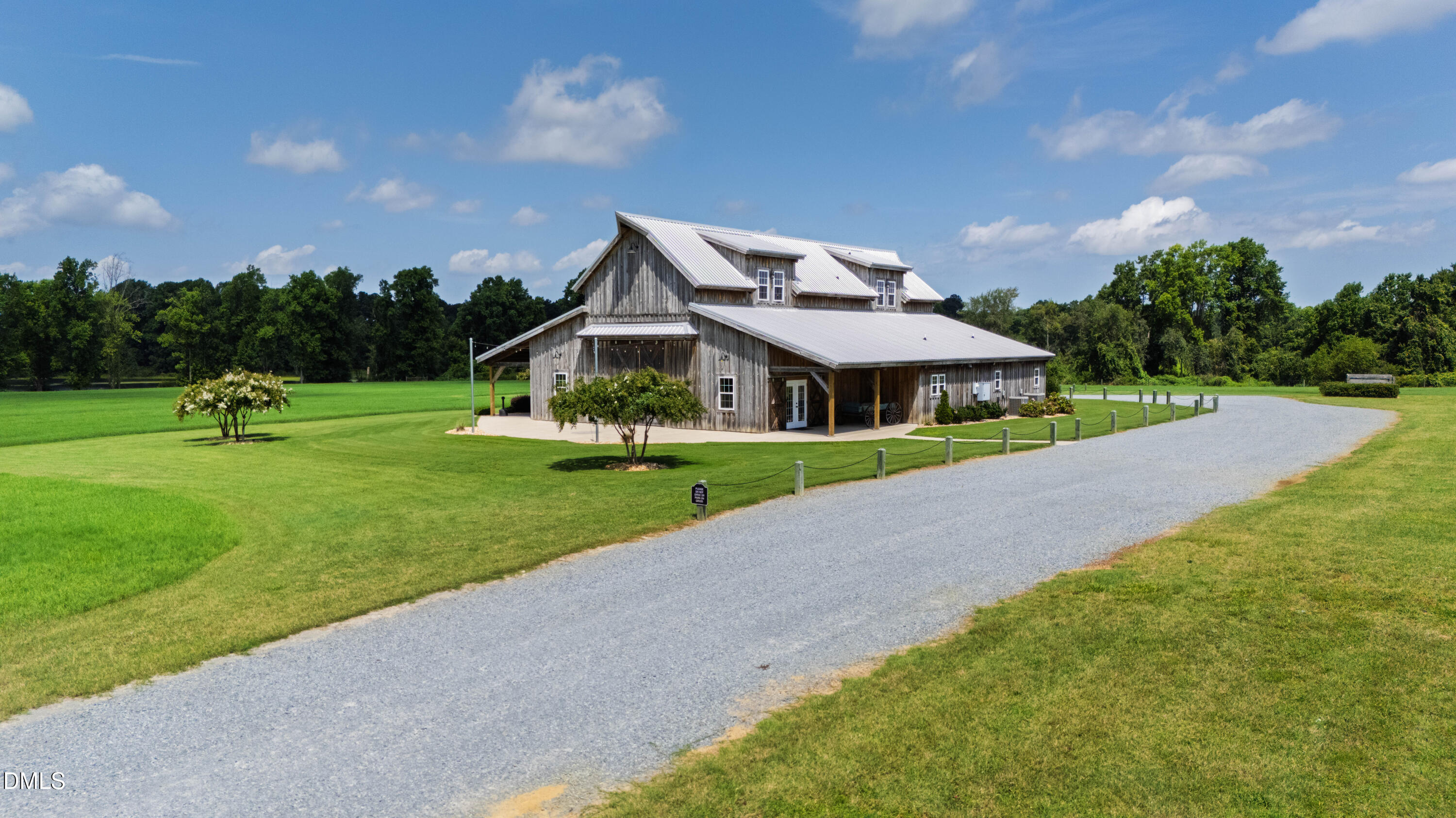 Weathered-wood barn-style building with a metal roof, green lawn, and curving gravel drive.