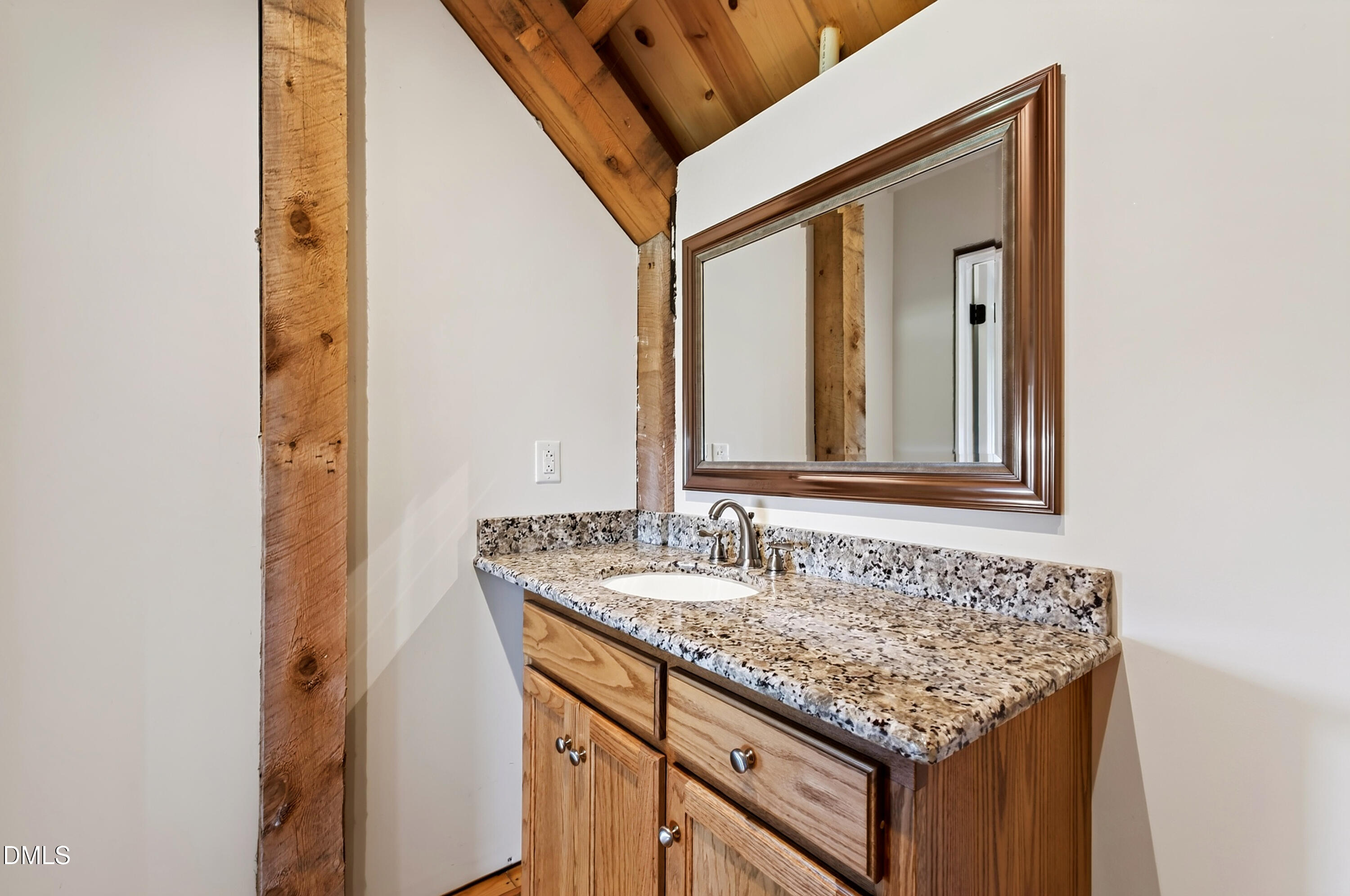 Bathroom vanity with a speckled granite counter, wooden cabinetry, and a large framed mirror.