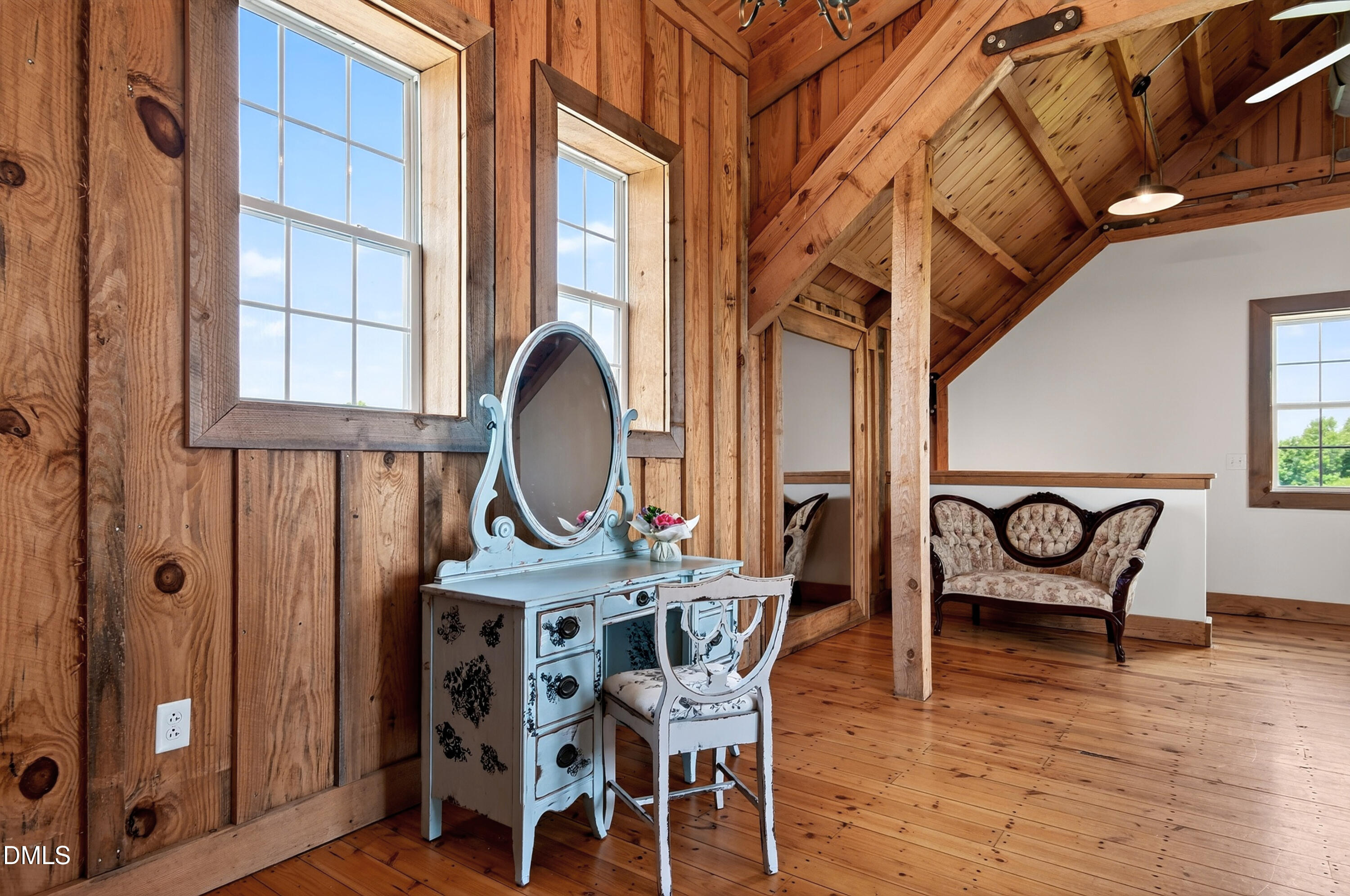 Furnished timber loft with a pale blue vanity, large windows, vaulted ceiling, and upholstered loveseat.