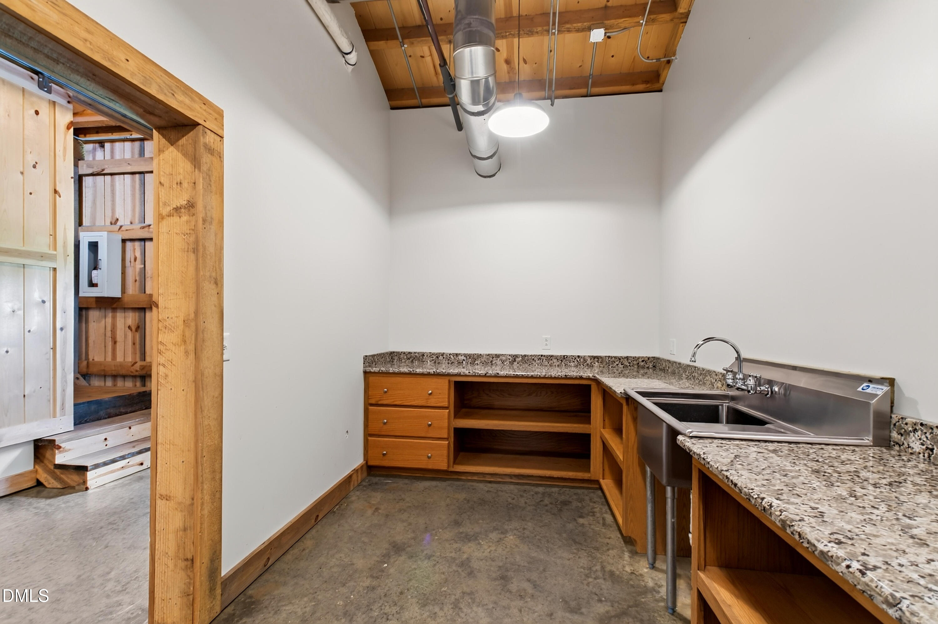 Utility room with a deep stainless steel sink, open wooden cabinetry, and exposed ceiling ductwork.