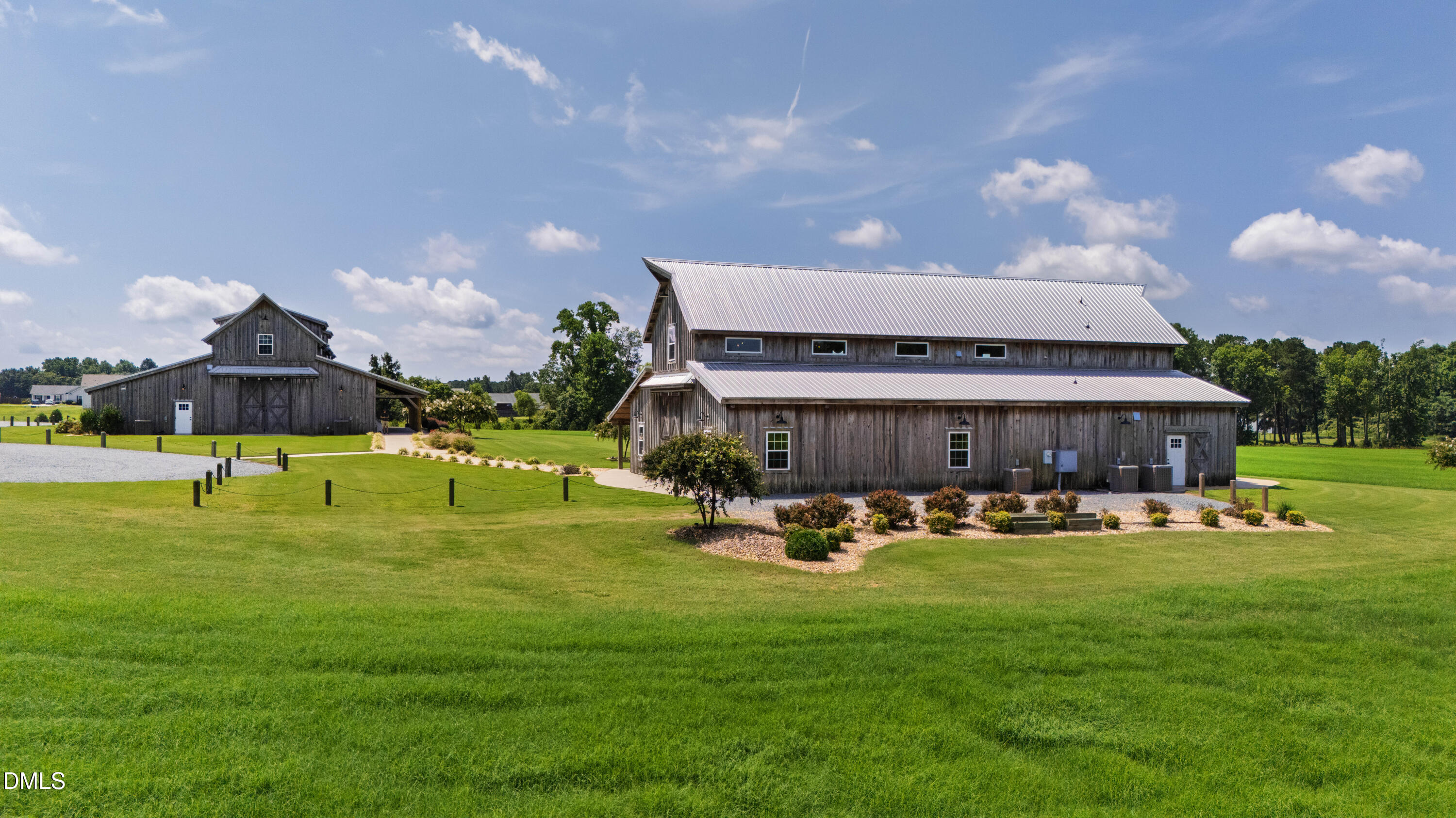 Two rustic timber buildings with metal roofs stand beside a broad green lawn.