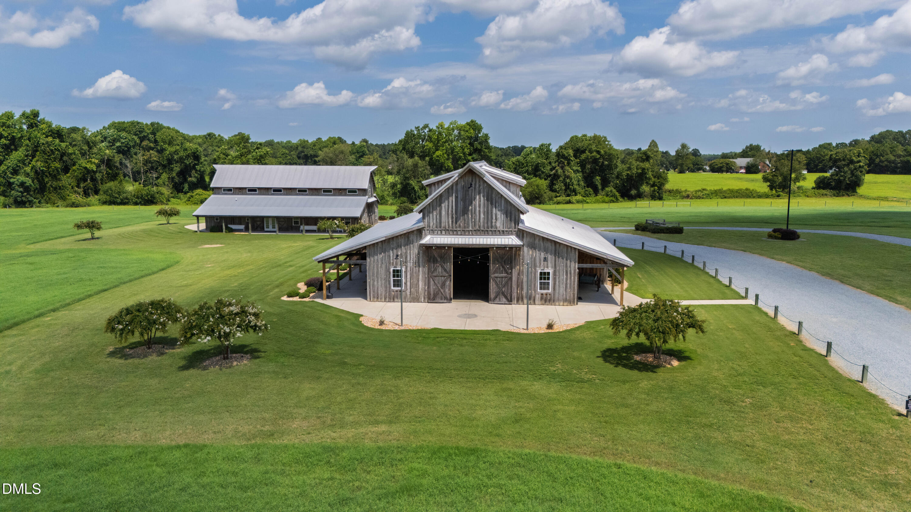 Rustic wooden barn with covered wings and a gravel drive across expansive green lawns.
