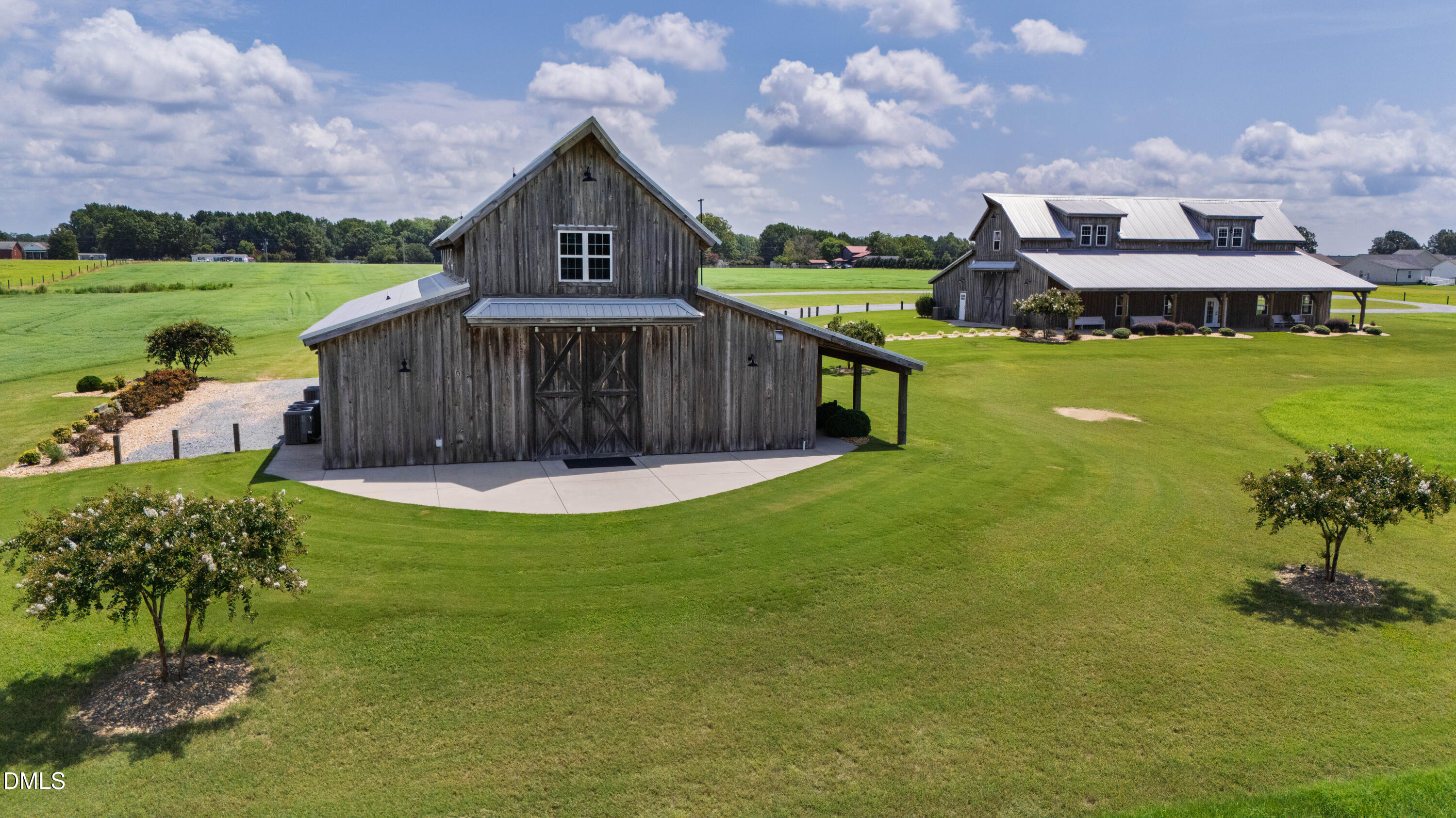 Aerial view of two timber buildings with metal roofs surrounded by expansive lawn and open fields.