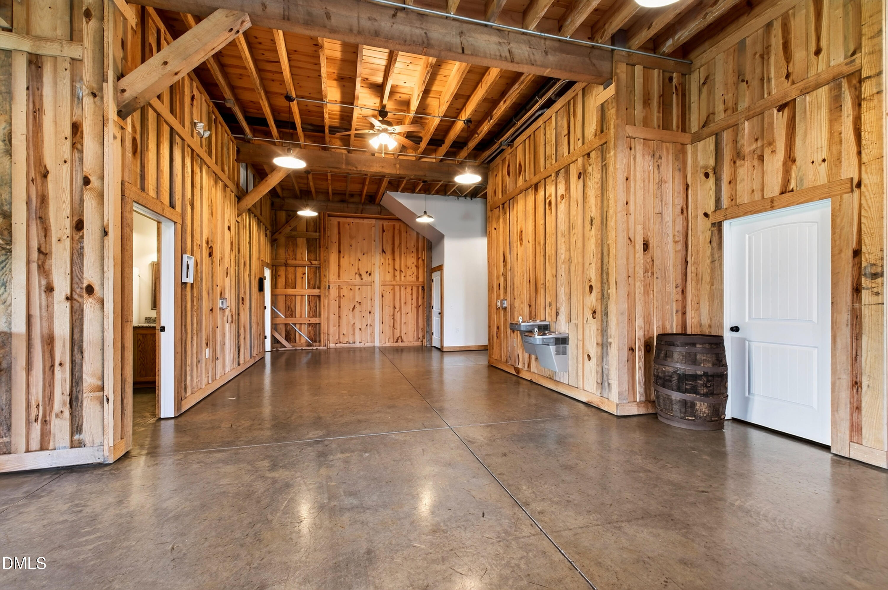 Rustic barn-style interior with exposed timber beams, concrete floor, drinking fountains, and a wooden barrel.