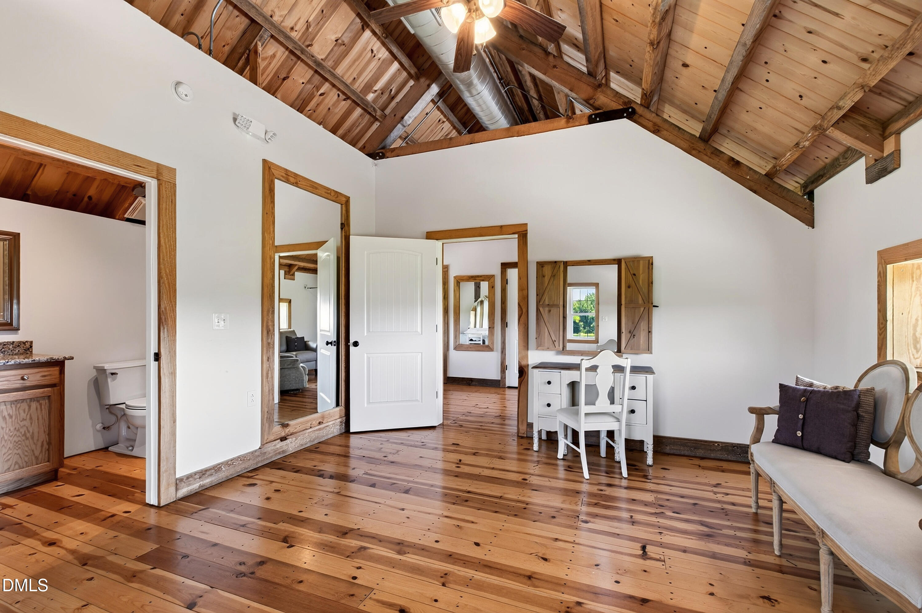 Furnished room with vaulted timber ceiling, wood floors, white desk, and shuttered window.