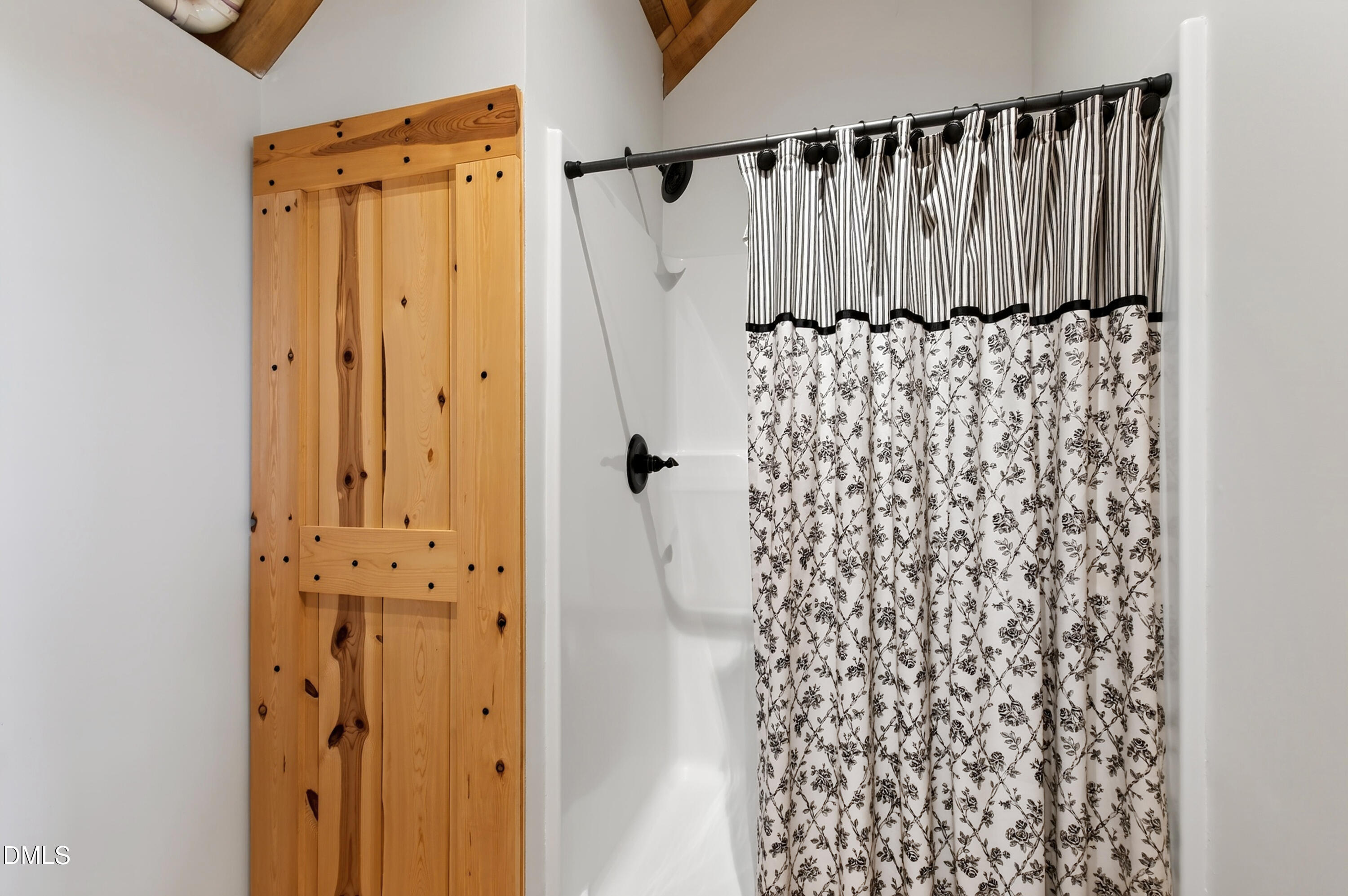 Bathroom with a floral shower curtain and rustic knotty-pine barn-style door.