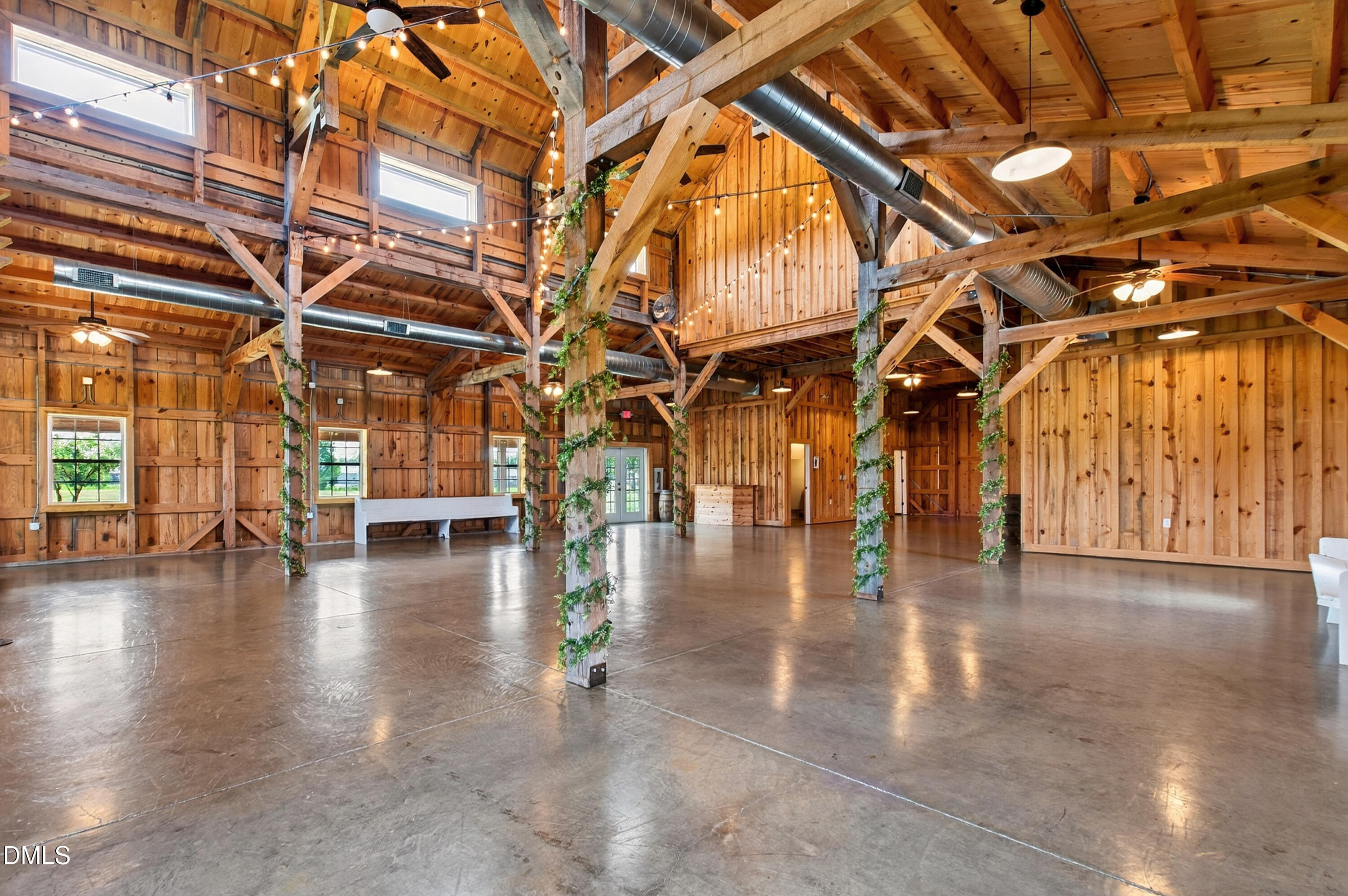 Open barn interior with exposed timber beams, string lights, and a polished concrete floor.